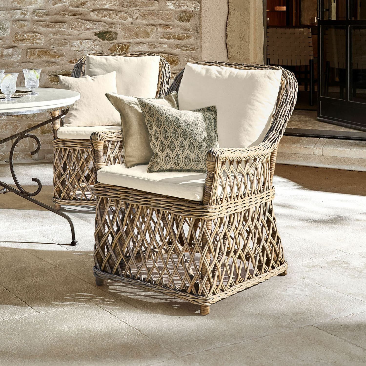 Sillón Nesvryn Sillón cómodo de ratán natural con cojines crema y cojines decorativos para terraza elegante.
