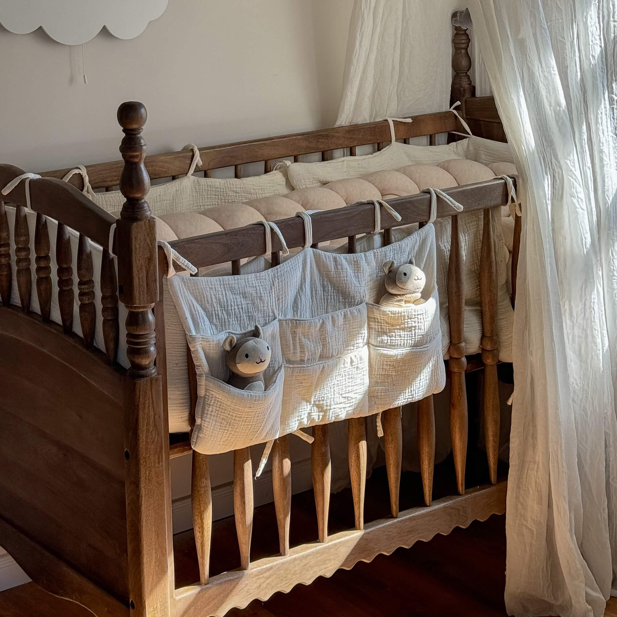 Cuna de madera con protector de algodón crema y peluches en los bolsillos para habitación infantil