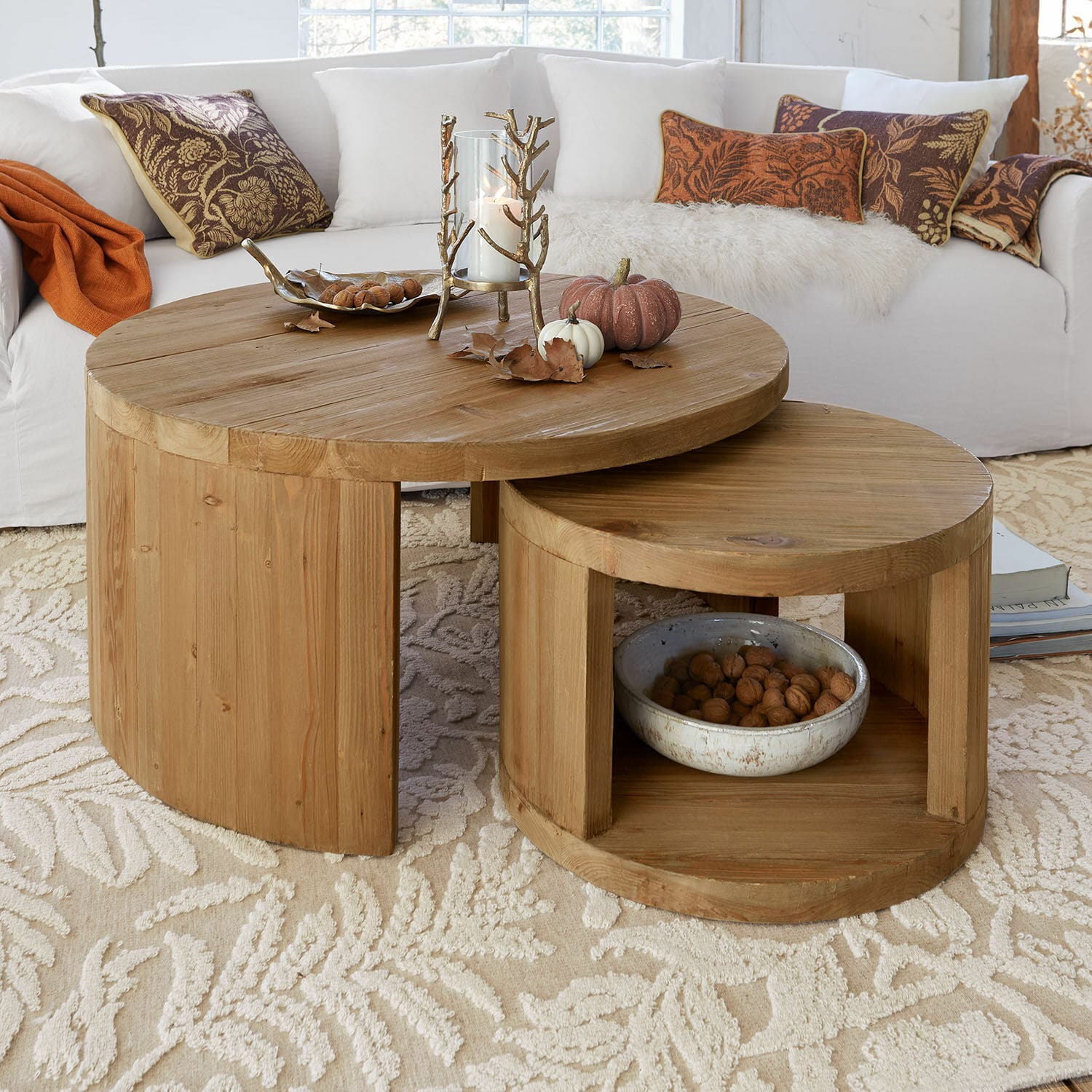 Dos mesas de centro redondas de madera de pino natural sobre alfombra clara con decoración otoñal