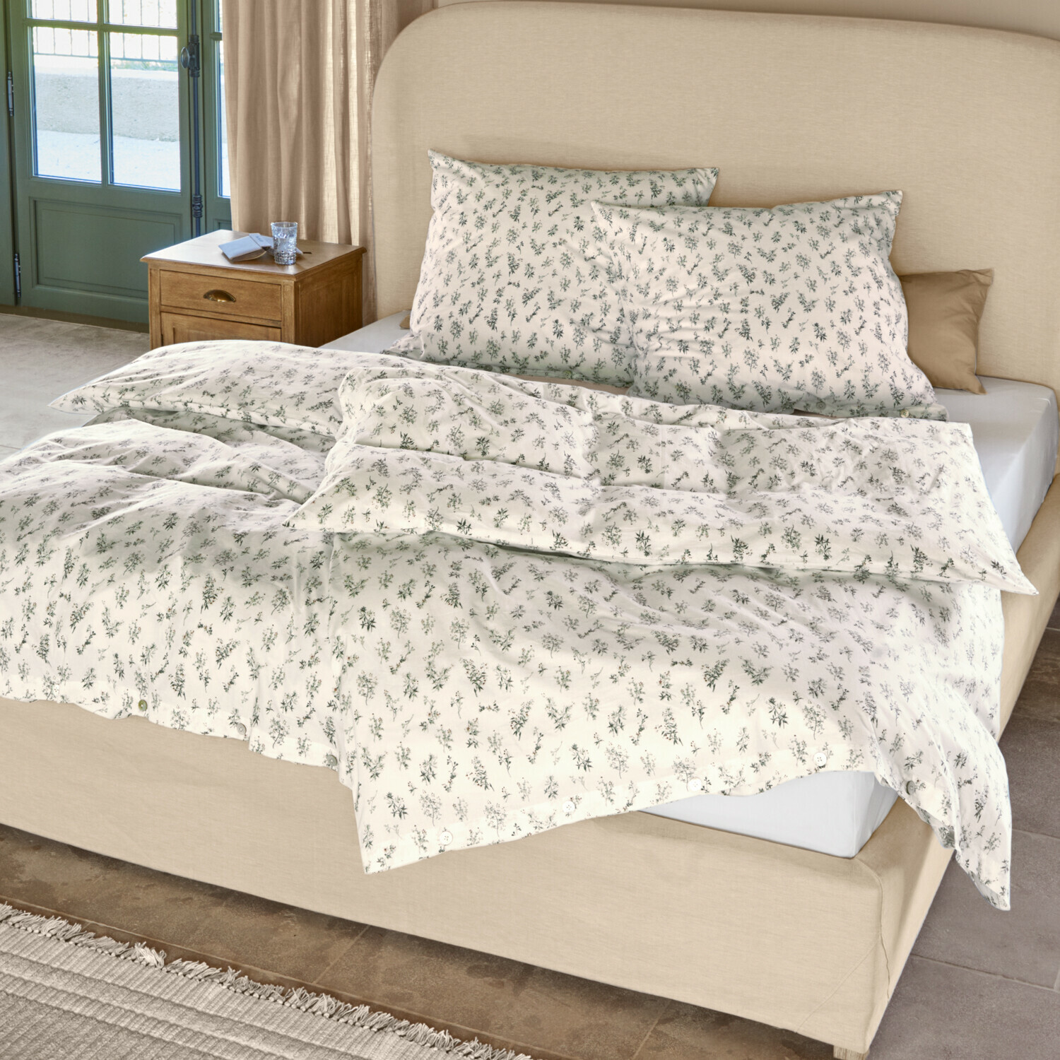 Ropa de cama Somerlyn Ropa de cama de algodón color crema con delicado estampado vegetal verde sobre cama con cabecero beige