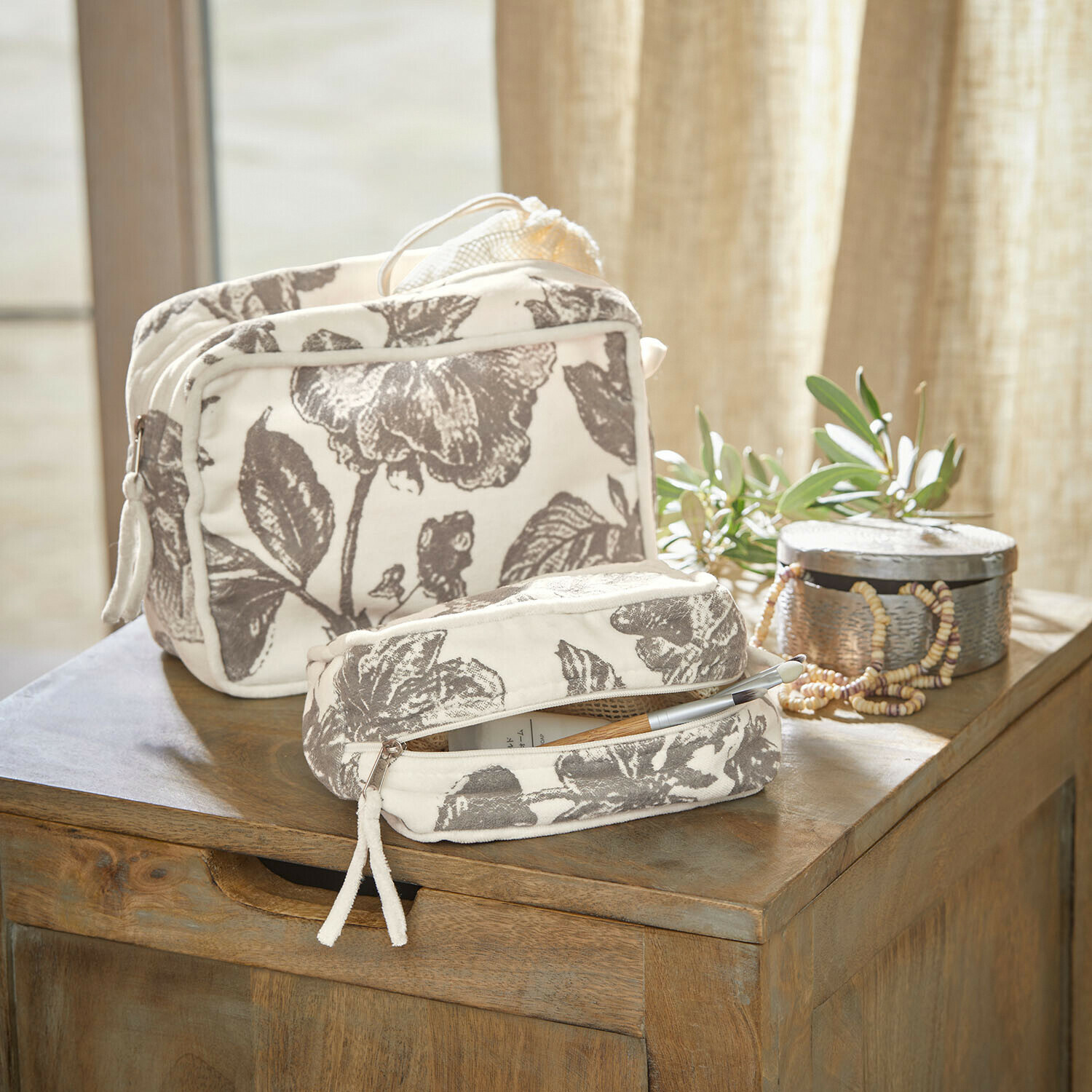 Set de 2 bolsitas Brilonne Conjunto de dos neceseres de algodón color crema con estampado floral gris sobre mesa de madera