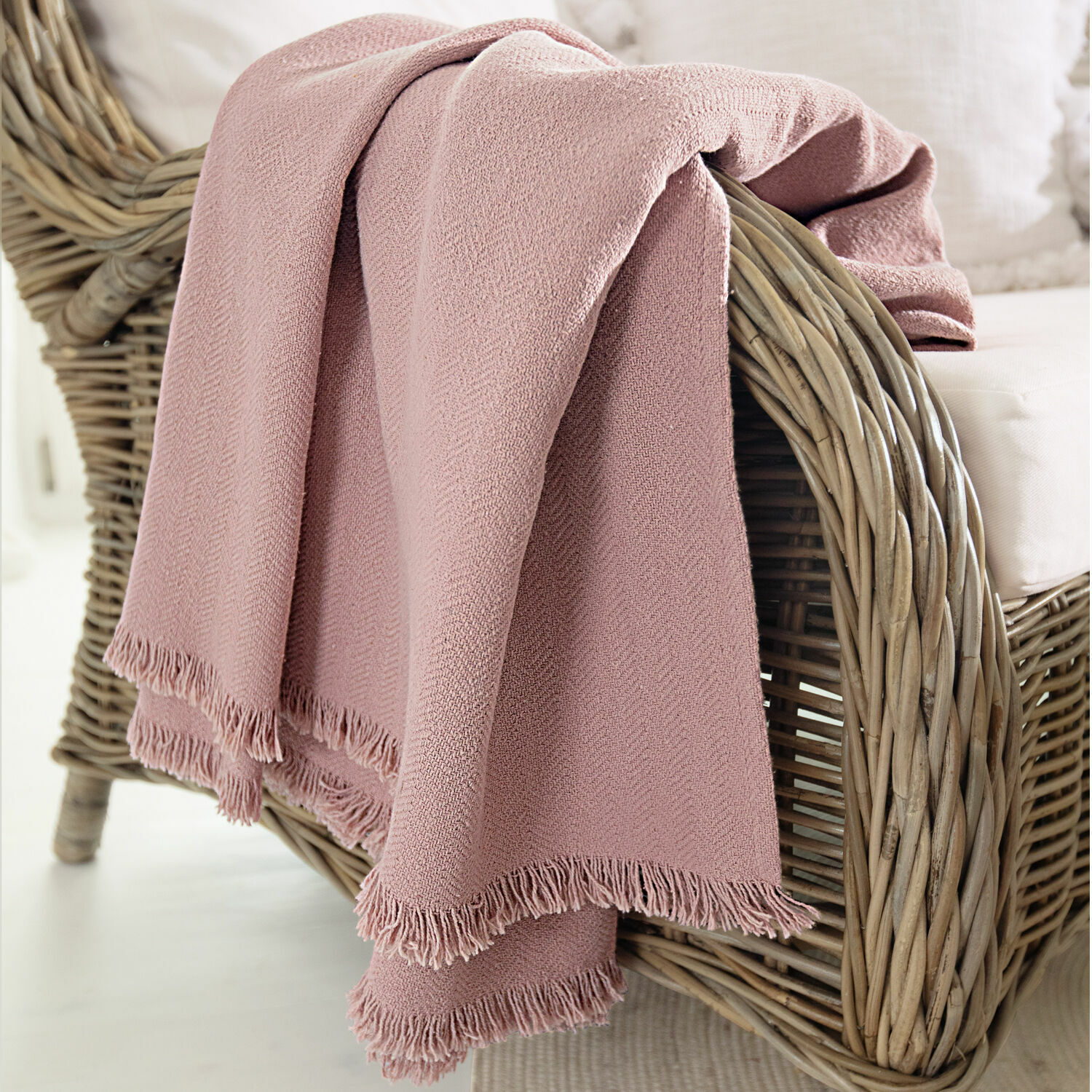 Plaid Herepian Manta rosa de material suave con flecos sobre sillón de mimbre para sala de estar