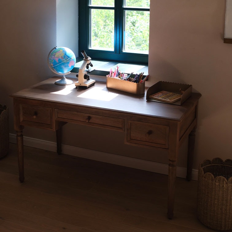 Escritorio de madera con tres cajones junto a la ventana, globo terráqueo y microscopio sobre la superficie
