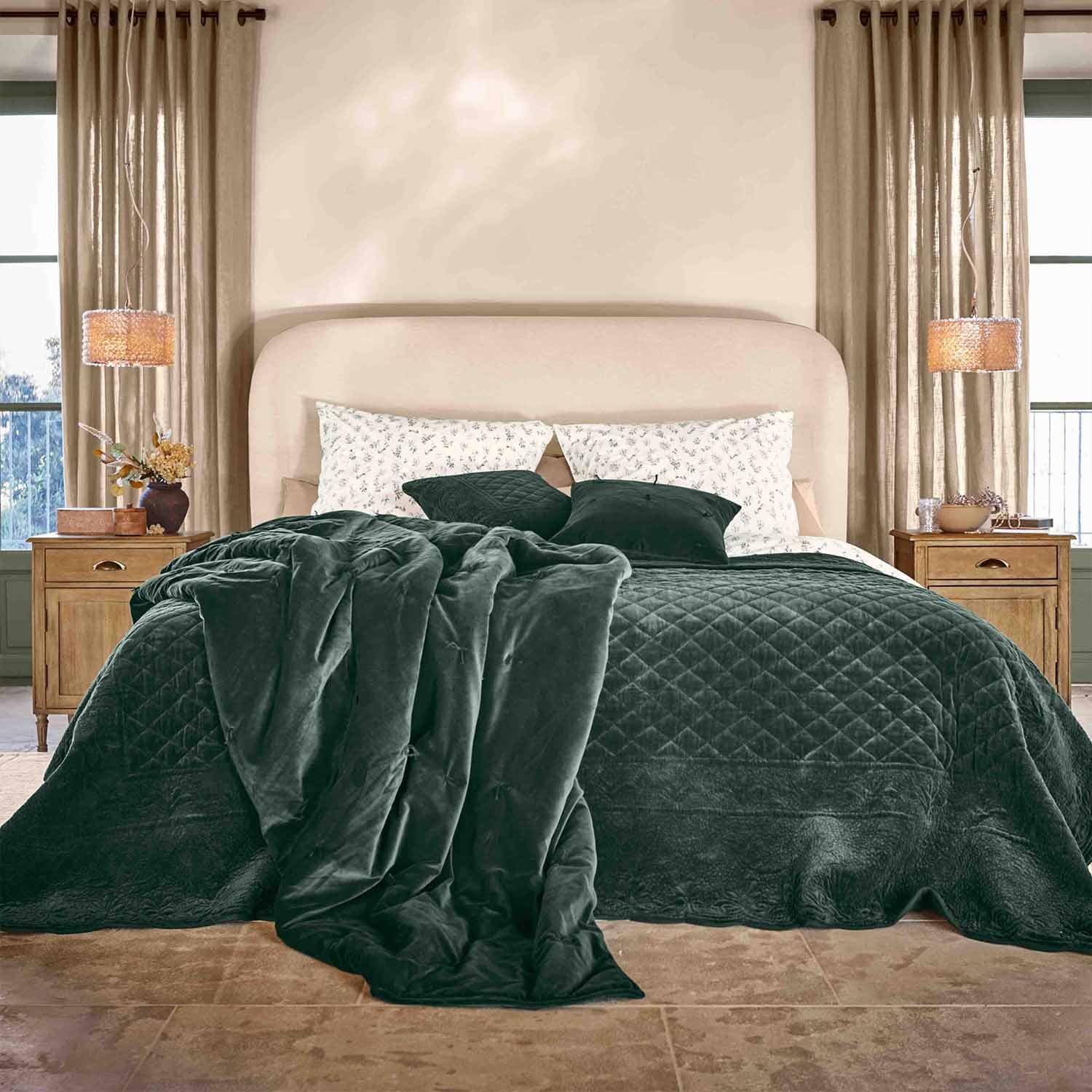 Manta y cojines de terciopelo verde oscuro sobre cama con cabecero beige en dormitorio acogedor