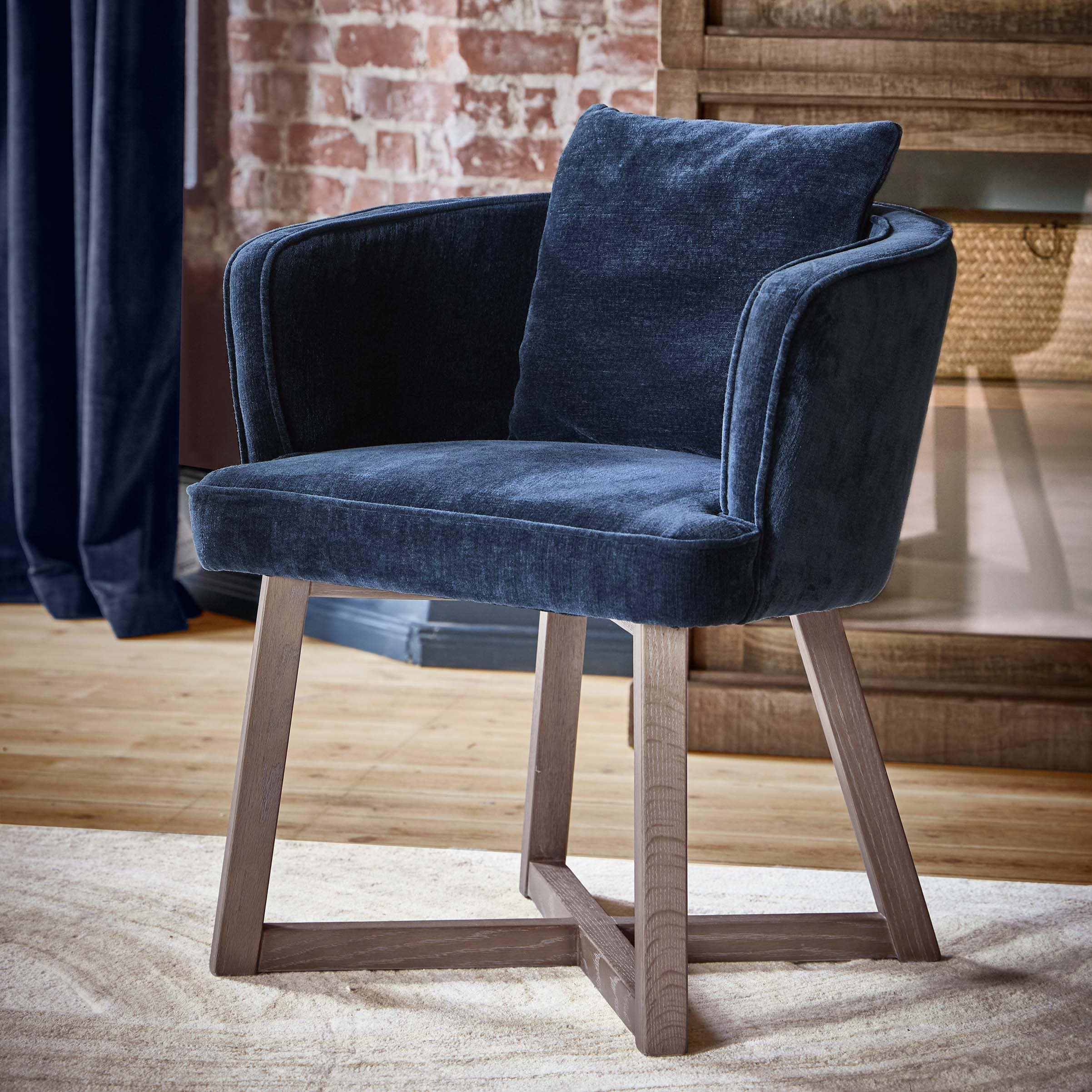 Sillón azul marino de tela suave con patas de madera en interior elegante con pared de ladrillo