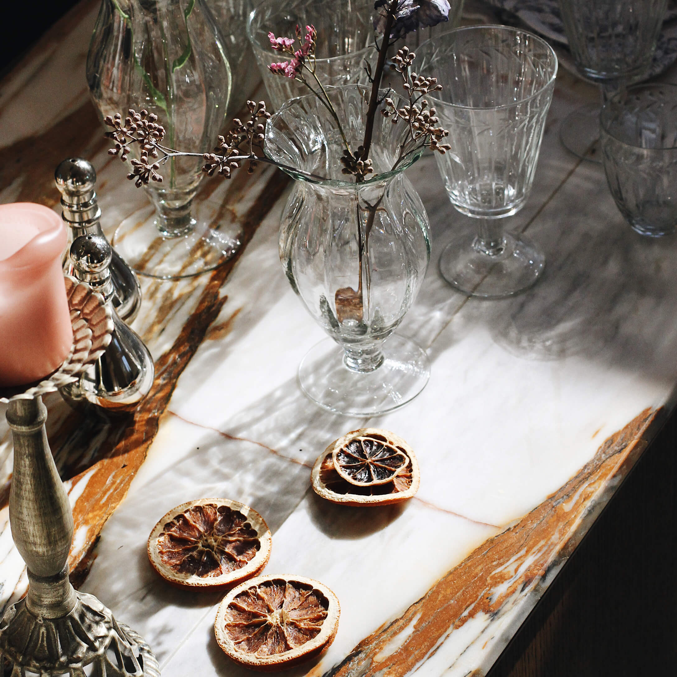 Jarrón de cristal con flores secas sobre encimera de mármol con rodajas decorativas de fruta seca