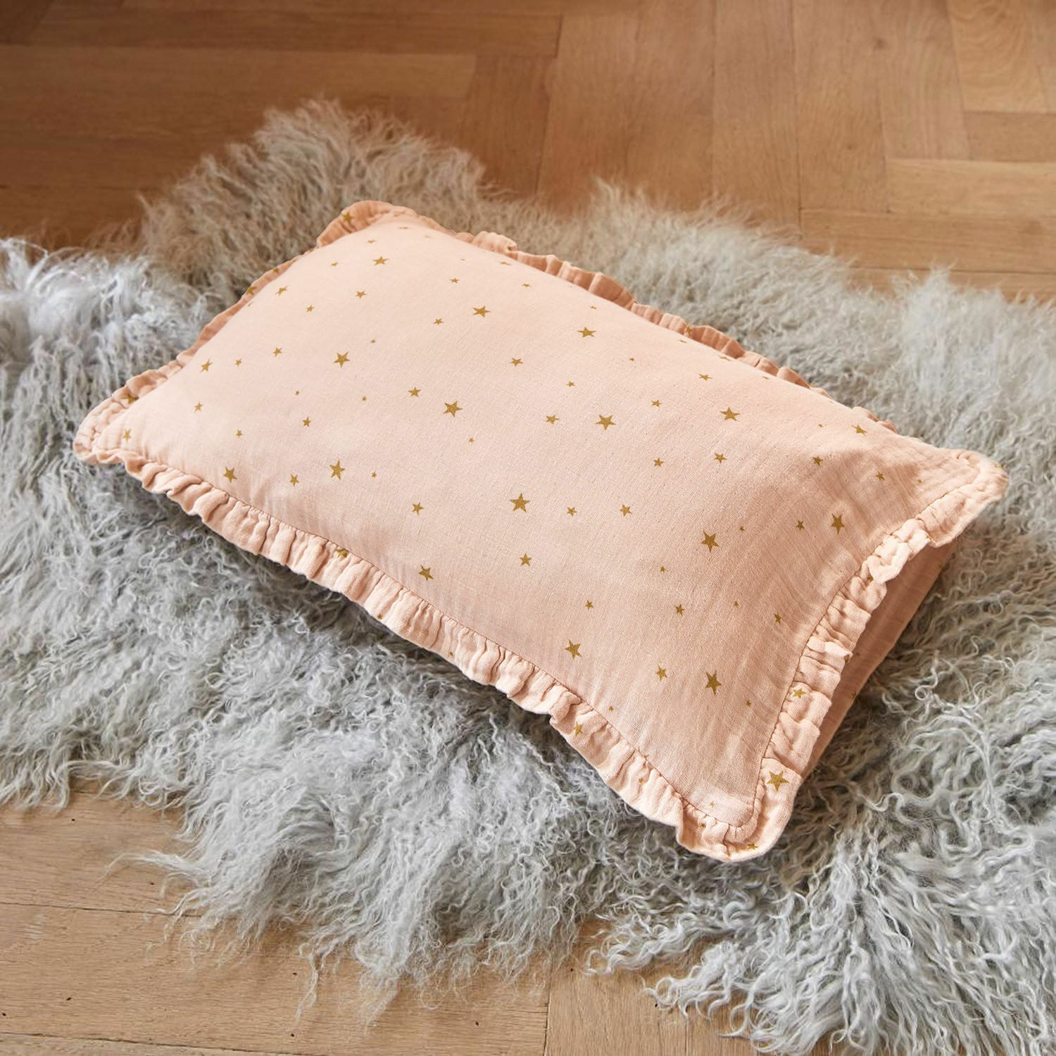 Funda de cojín Vianne Cojín rosa de algodón con volantes y estrellas doradas sobre alfombra gris de piel sintética