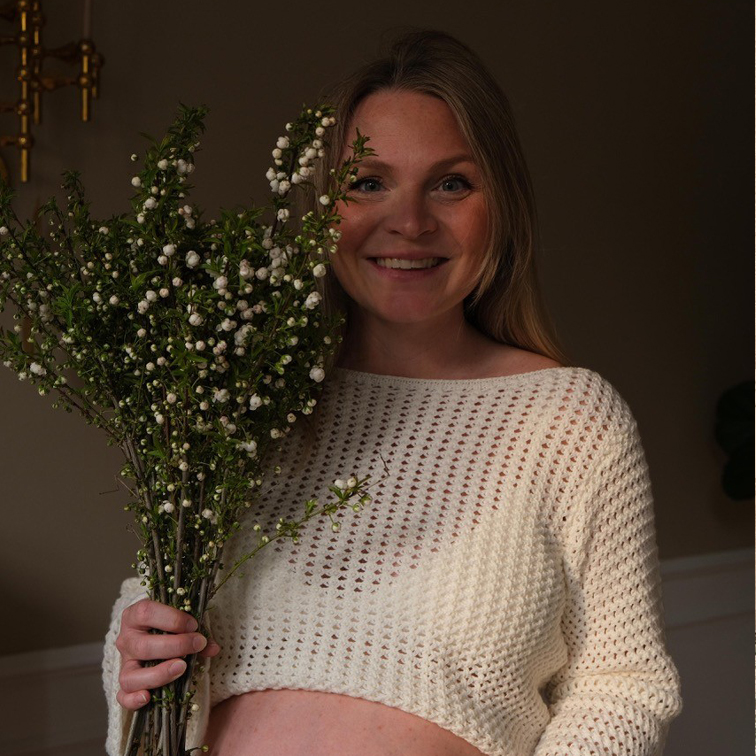 Mujer con suéter blanco calado sosteniendo ramas con flores blancas, decoración natural para el hogar