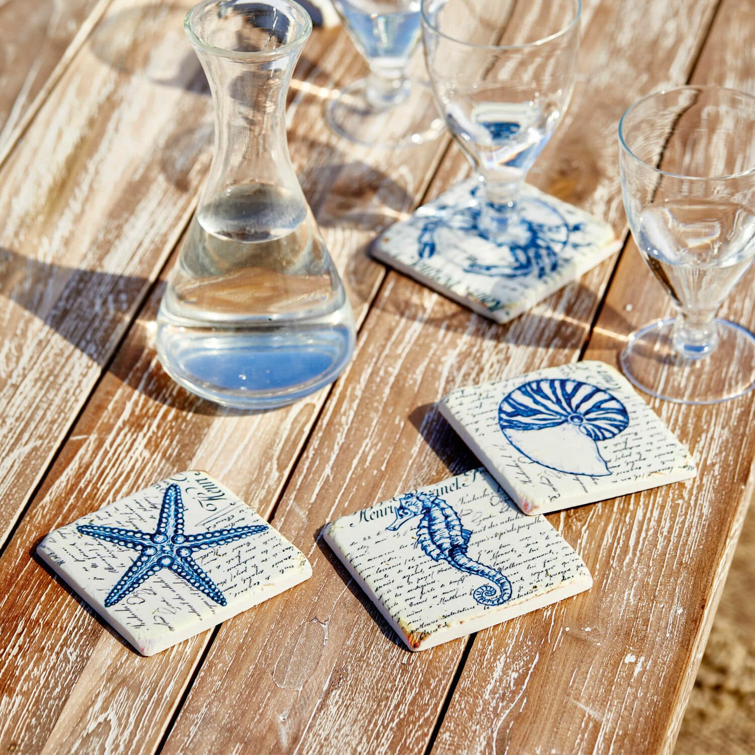 Set de 4 posavasos Faune Marine Posavasos de cerámica con motivos marinos azules sobre mesa de madera, decoración de mesa