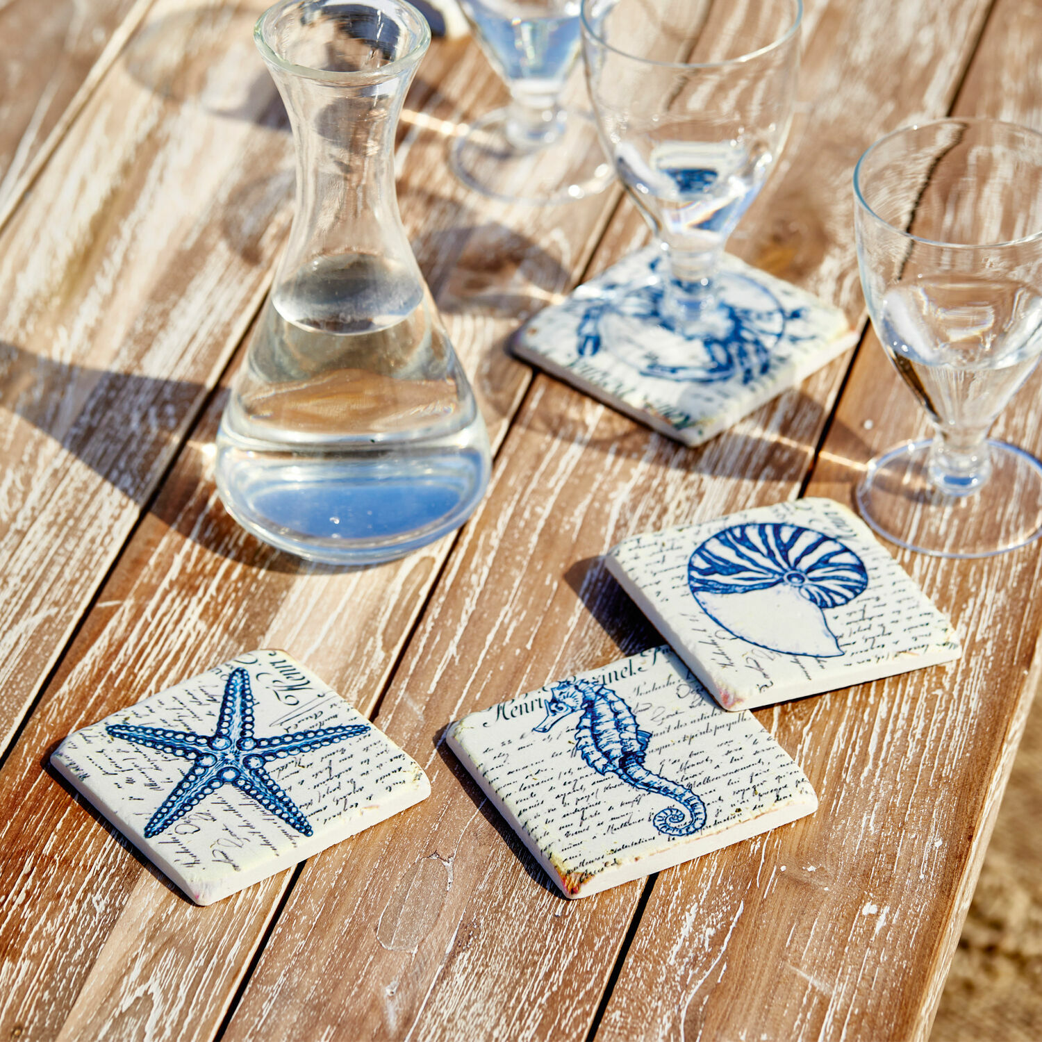 Set de 4 posavasos Faune Marine Posavasos de cerámica con motivos marinos azules sobre mesa de madera, decoración de mesa