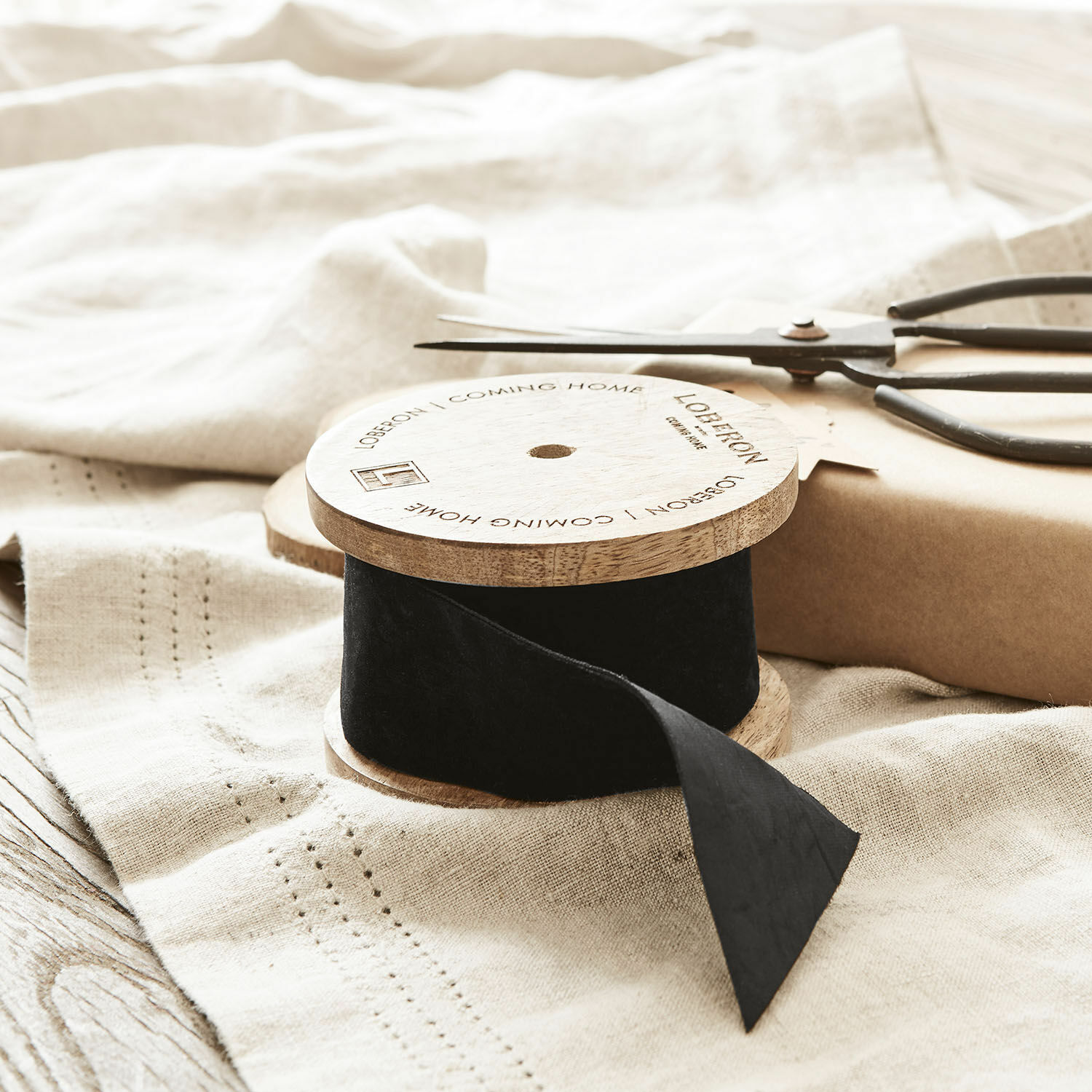 Cinta negra de terciopelo en carrete de madera sobre tela de lino con tijeras para envolver