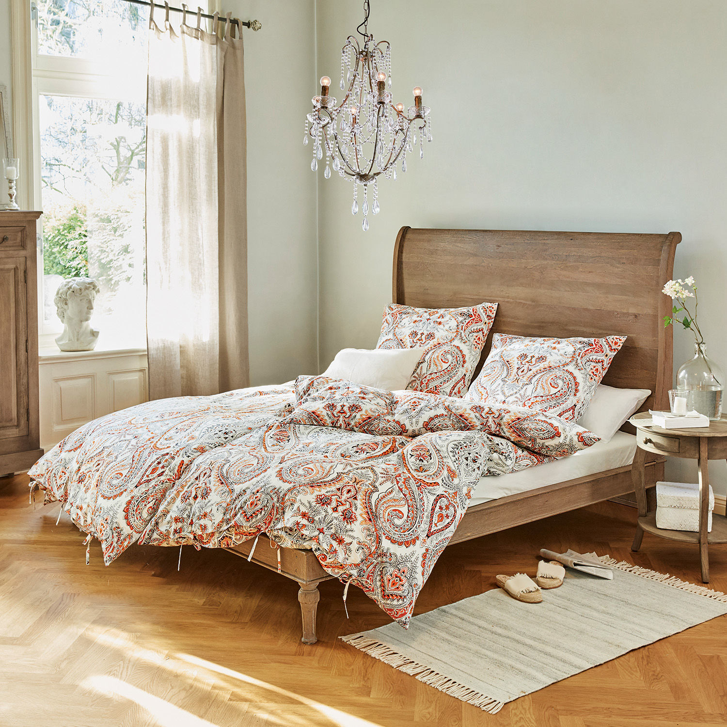 Cama Saint-Germier Dormitorio con cama de madera y ropa de cama con patrón paisley rojo y blanco, alfombra y lámpara de cristal