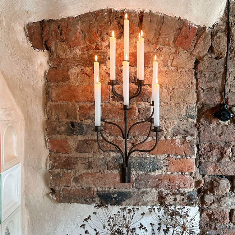 Candelabro de pared de metal con siete velas blancas encendidas sobre pared de ladrillo, decoración interior