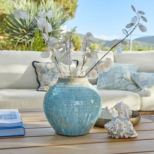Jarrón de cerámica azul sobre mesa de madera con decoración de plantas secas y conchas, decoración interior elegante