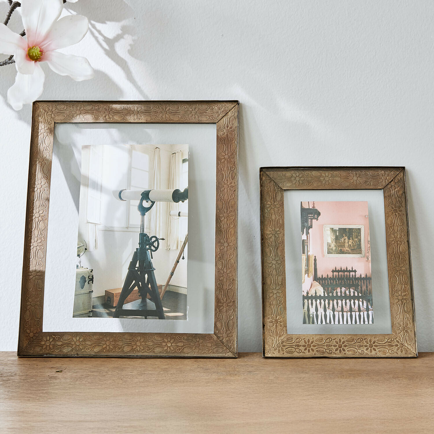 Set de 2 marcos Viadora Dos marcos de fotos decorativos de latón con diseño floral sobre mesa de madera