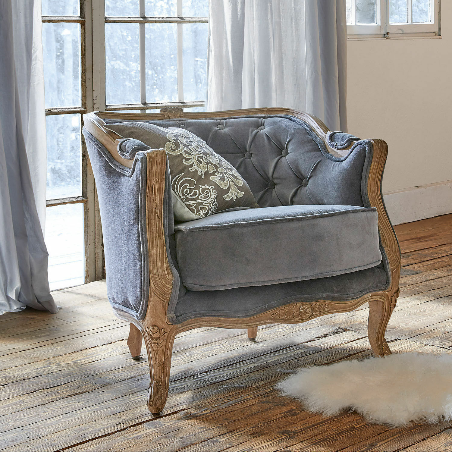 Sillón Annezay Sofá gris de terciopelo con marco de madera tallada sobre suelo de madera en habitación luminosa