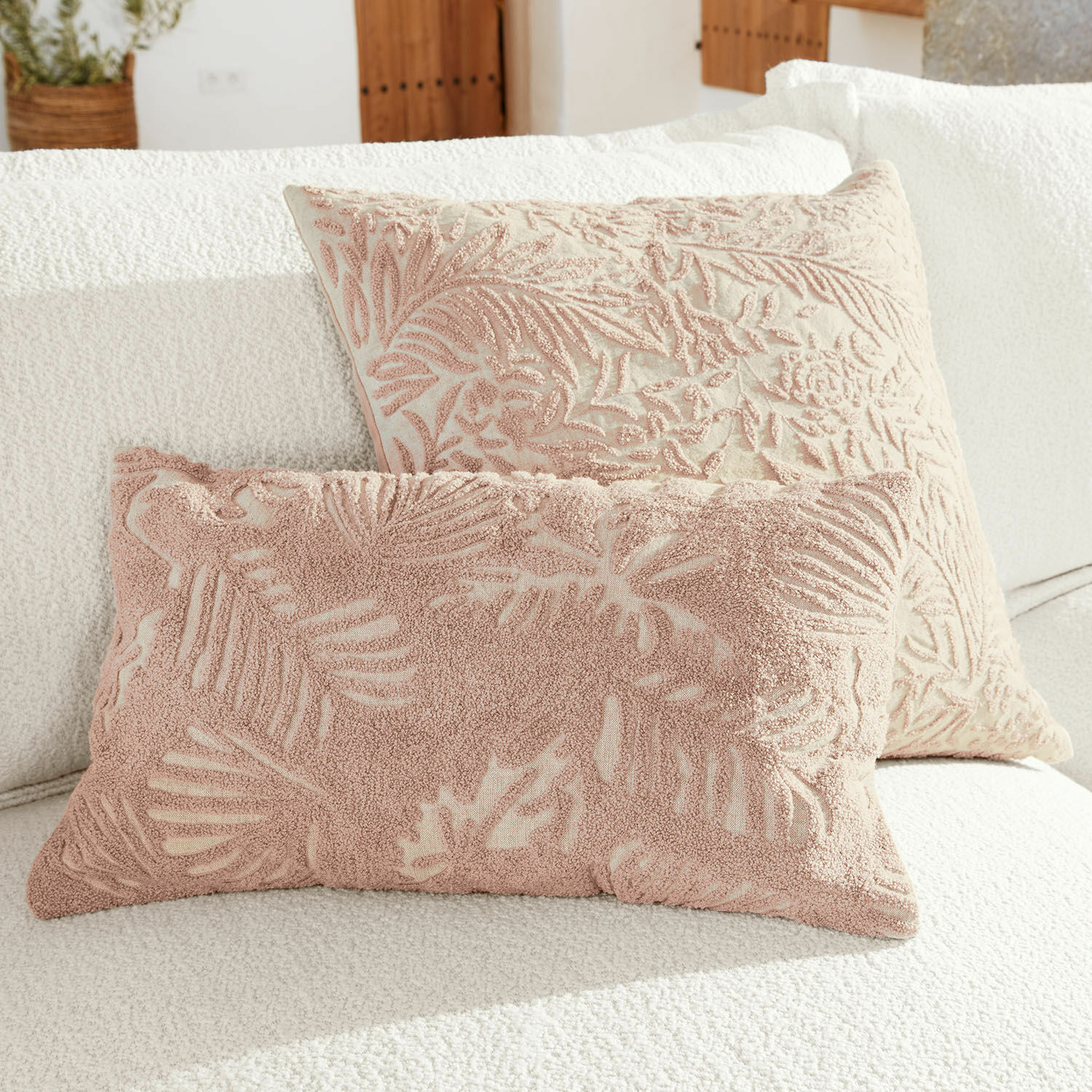Set de 2 fundas de cojín Enchanto Dos cojines decorativos con diseño de hojas rosas sobre fondo crema en sofá blanco