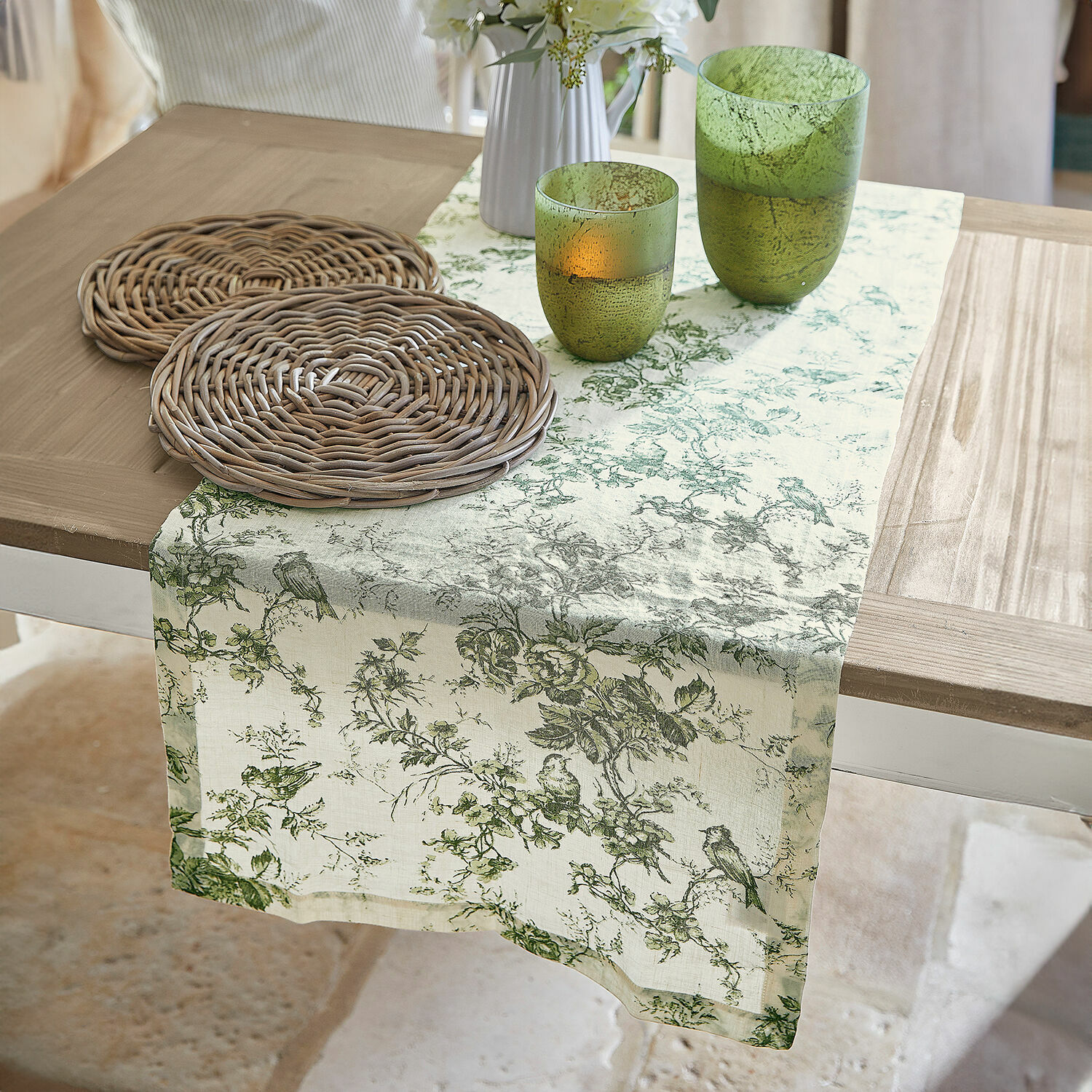 Camino de mesa Mercier Camino de mesa de lino con diseño vegetal verde sobre mesa de madera con posavasos de mimbre y vasos verdes