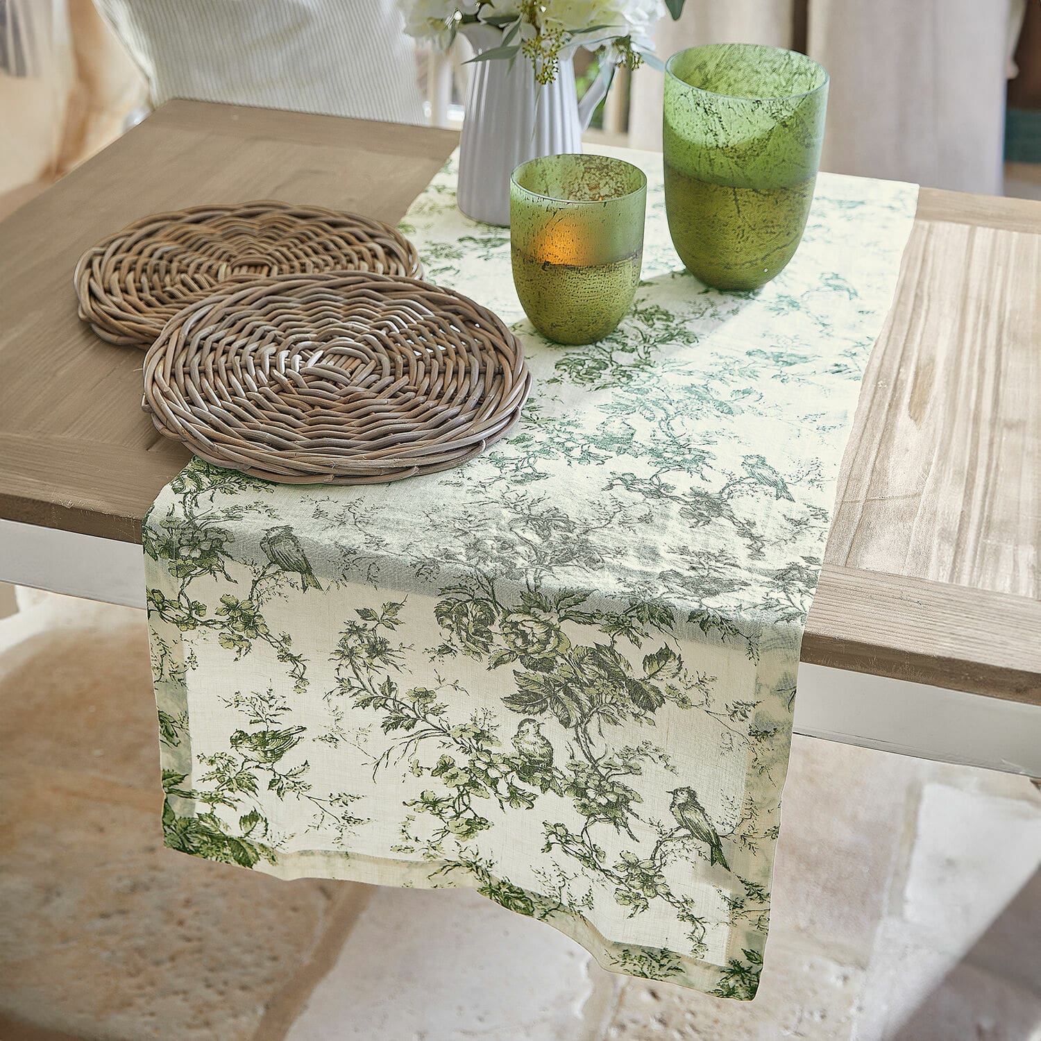 Camino de mesa Mercier Camino de mesa de lino con diseño vegetal verde sobre mesa de madera con posavasos de mimbre y vasos verdes