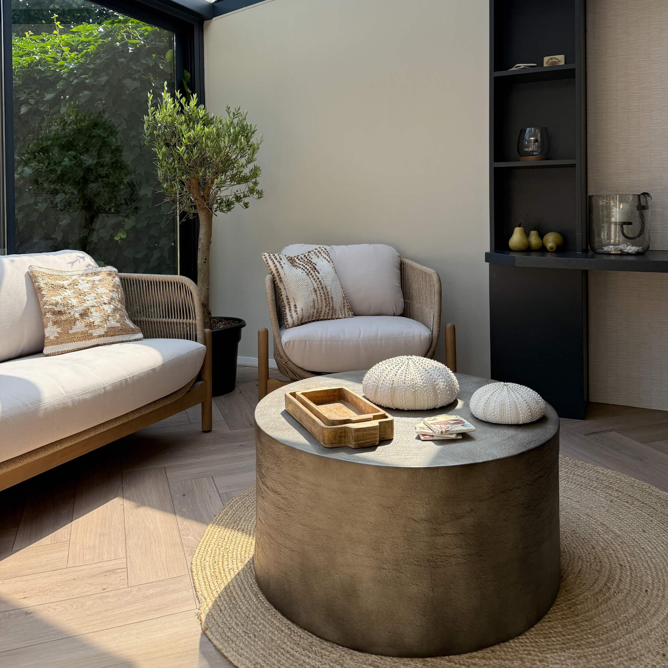 Salón moderno con sofá beige y sillón de tela, mesa de centro redonda de hormigón sobre alfombra natural