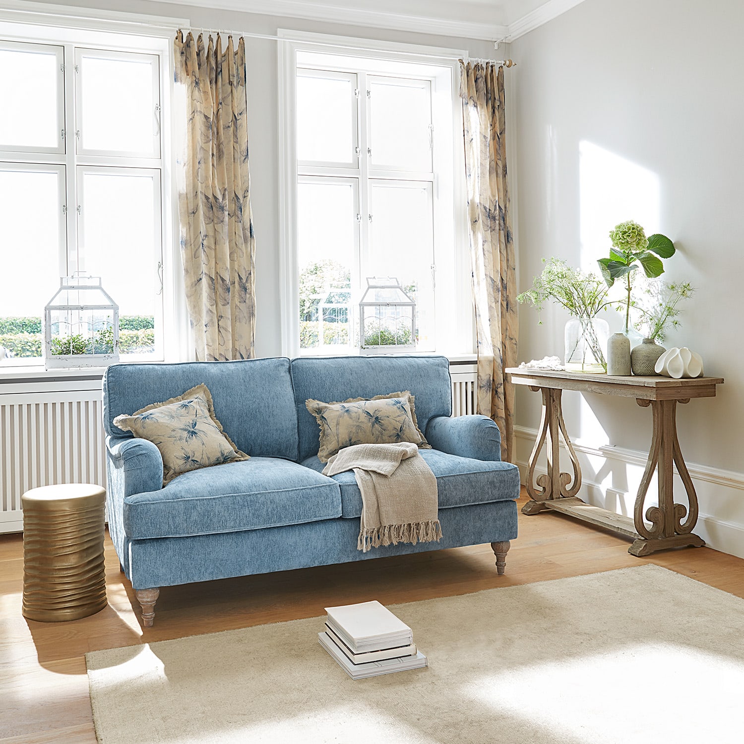 Sofá tapizado azul con cojines beige y mesa de madera en salón luminoso y moderno
