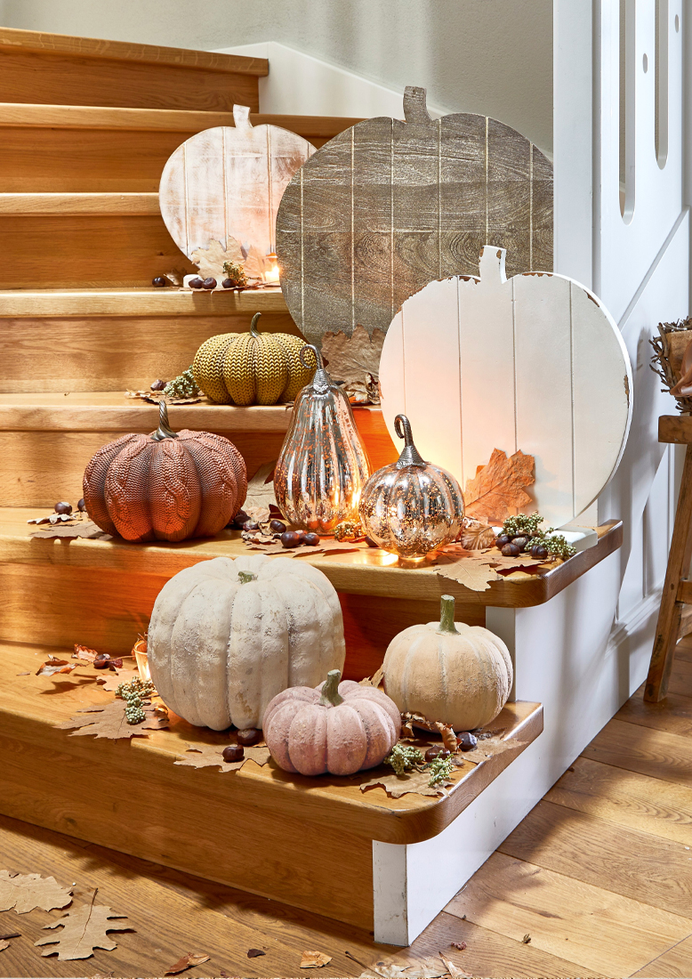 Decoración otoñal con calabazas de madera y tela en colores pastel sobre escalera de madera con hojas secas