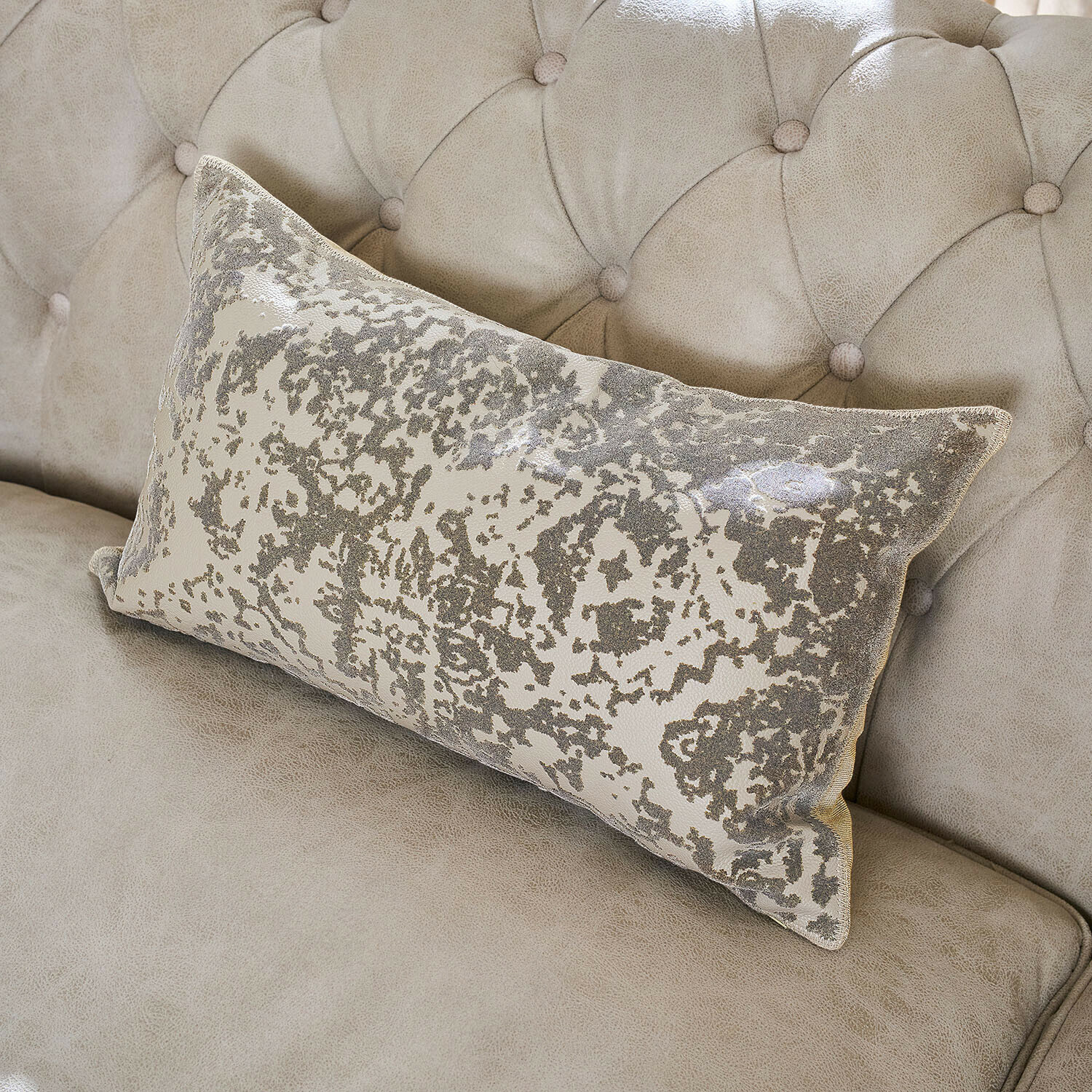 Cojín decorativo rectangular con patrón gris y beige sobre sofá beige claro acolchado