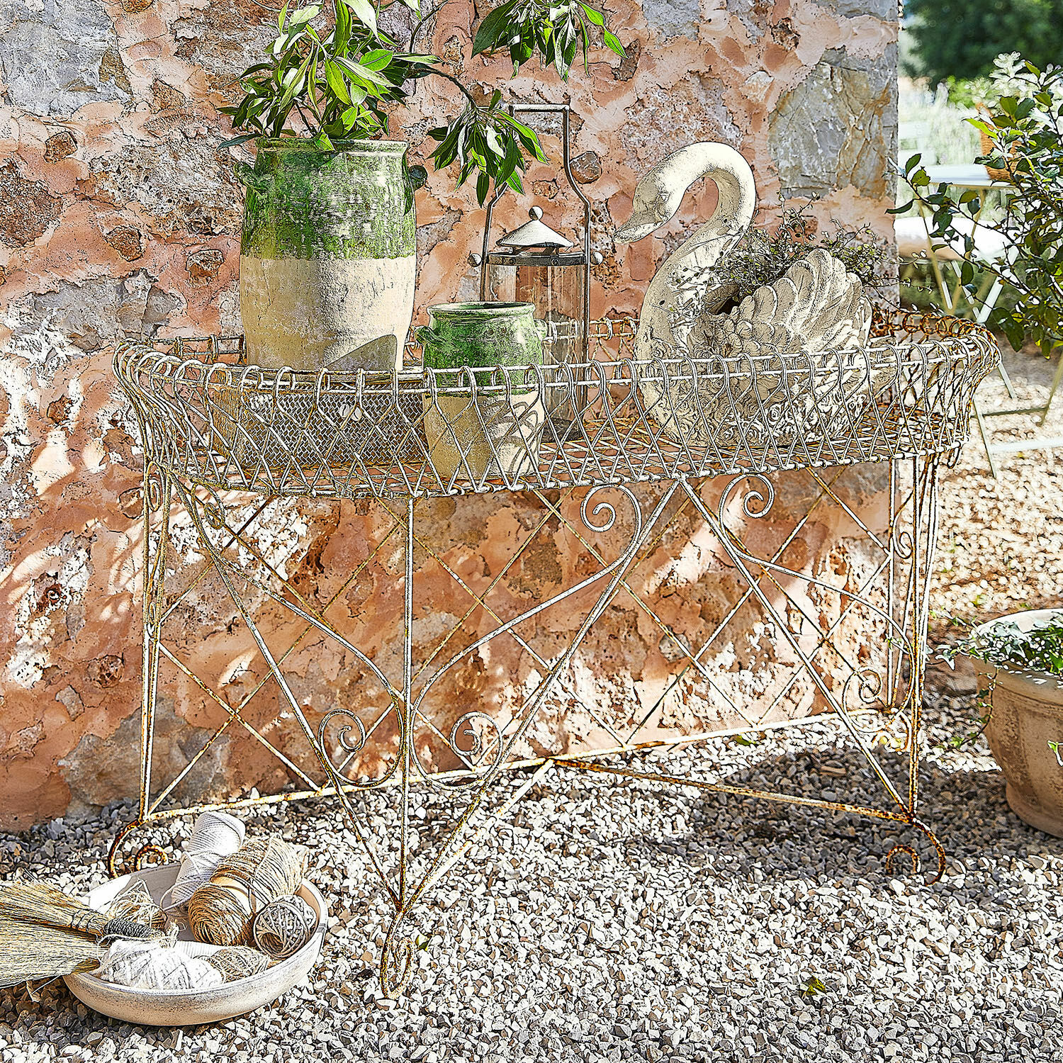 Estantería de jardín Pacentro Mesa de jardín rústica de metal con macetas decorativas y adorno de cisne frente a pared de piedra