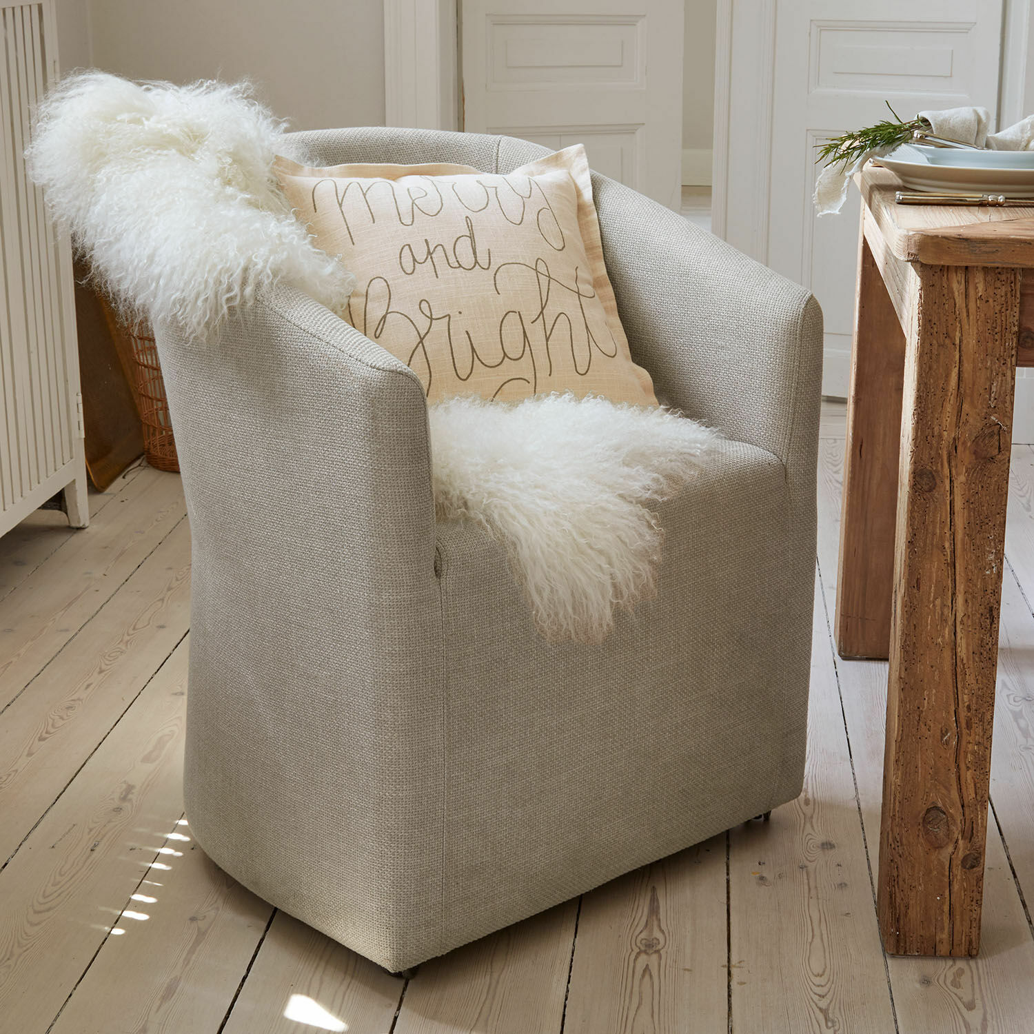 Sillón Holmsen Sillón tapizado gris con manta blanca suave y cojín decorativo claro en ambiente escandinavo