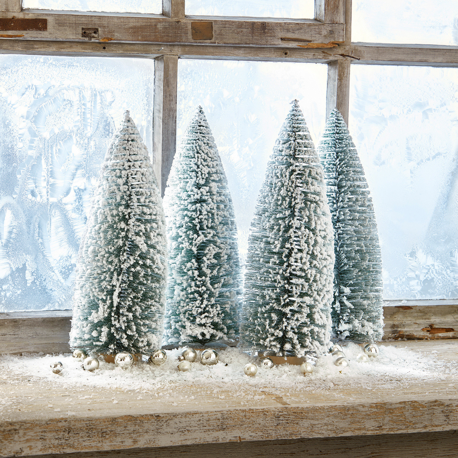 Set de 4 árboles decorativos Landscape Cuatro árboles de plástico verdes en forma cónica con nieve blanca sobre un alféizar de madera con bolas decorativas