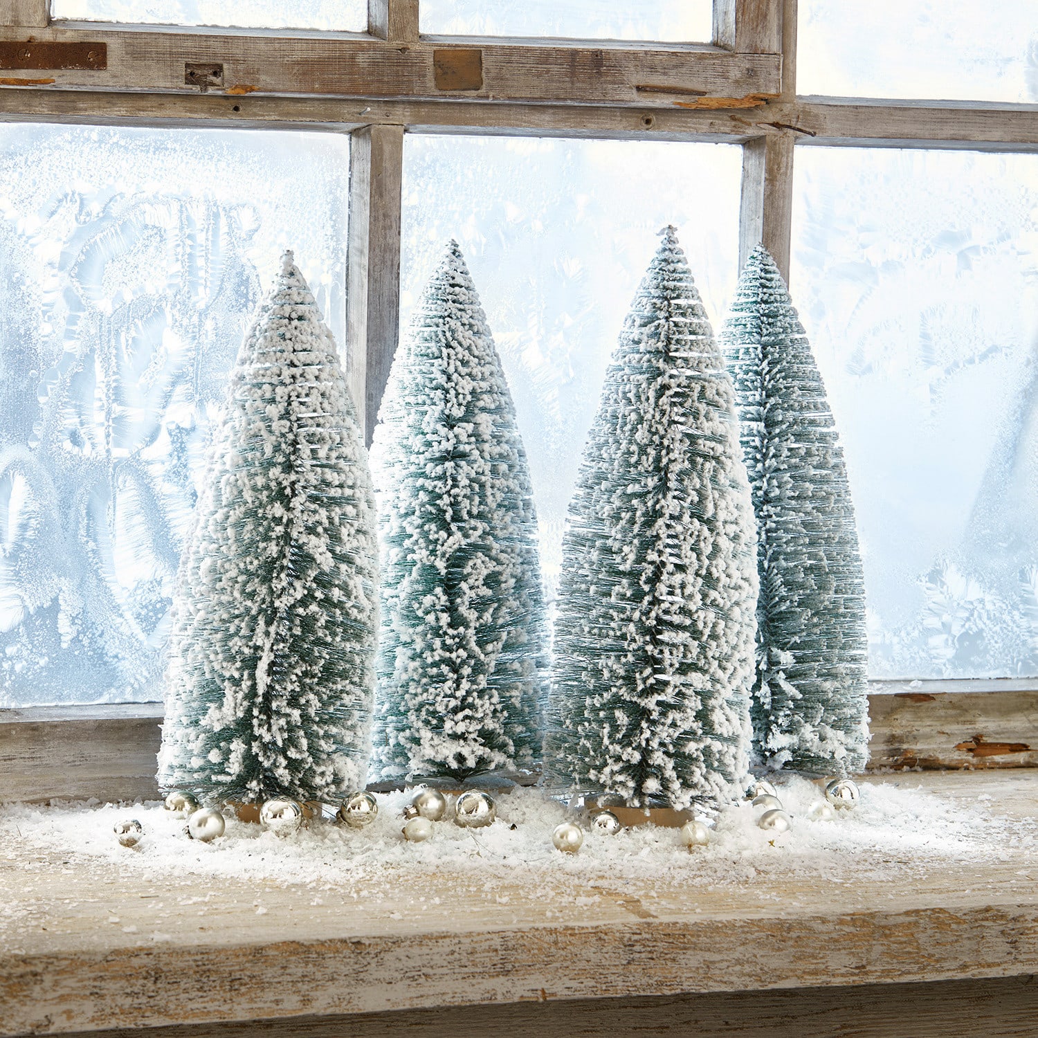 Set de 4 árboles decorativos Landscape Cuatro árboles de plástico verdes en forma cónica con nieve blanca sobre un alféizar de madera con bolas decorativas