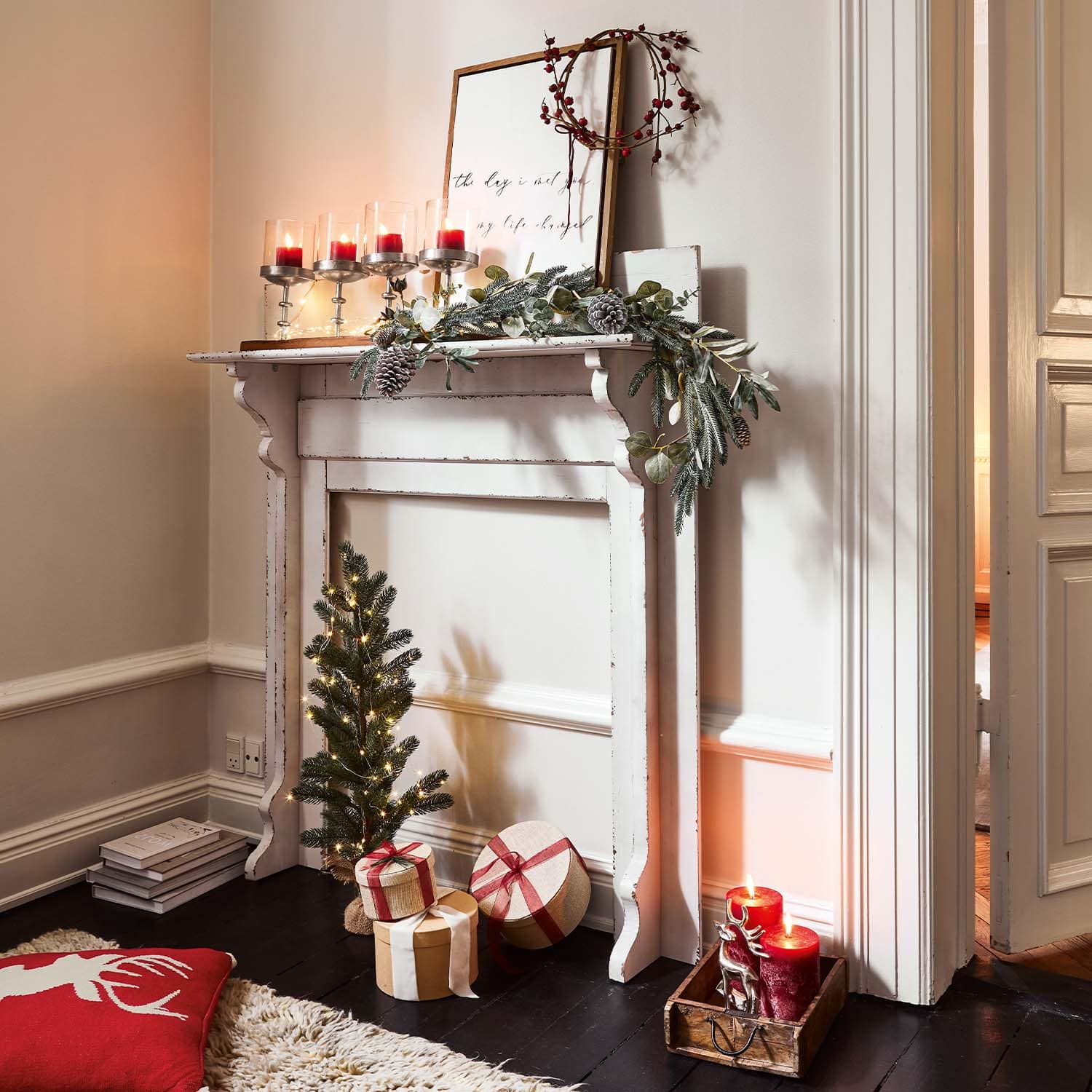Chimenea blanca de madera decorada para Navidad con velas rojas y regalos envueltos en el suelo