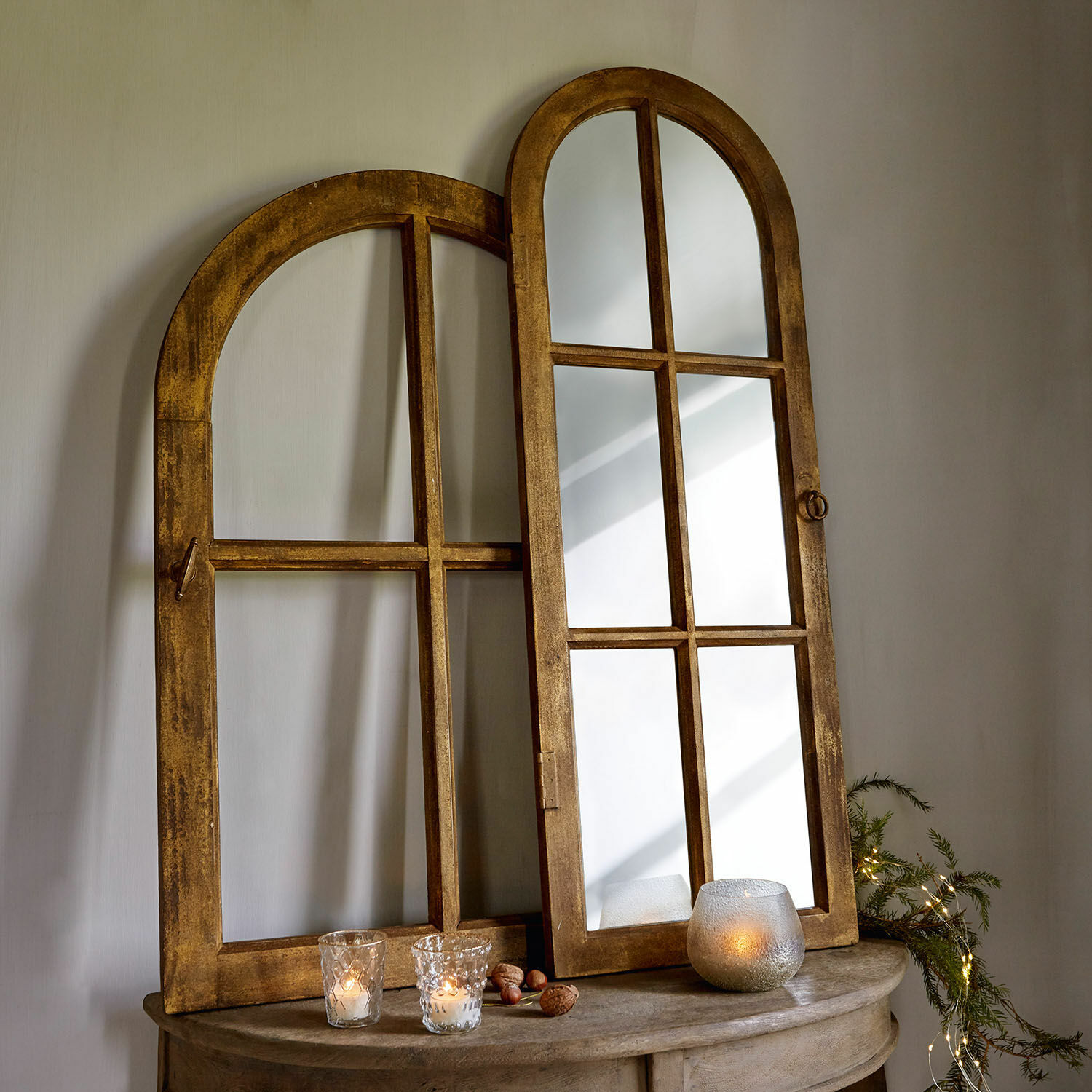 Espejo y ventana decorativa Crowley Espejo de madera con marco redondeado color miel sobre mesa con velas y decoración natural