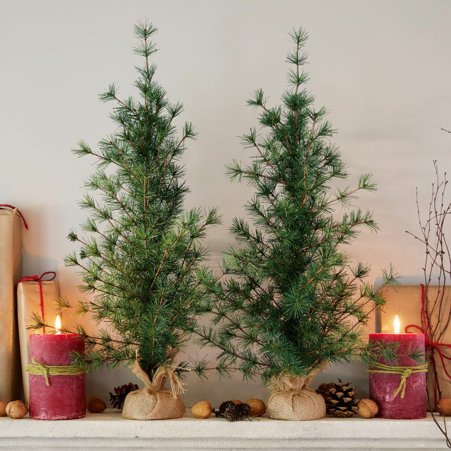 Set de 2 árboles decorativos Bohicon Dos pequeños árboles de Navidad verdes en sacos de yute con velas rojas y nueces sobre la chimenea