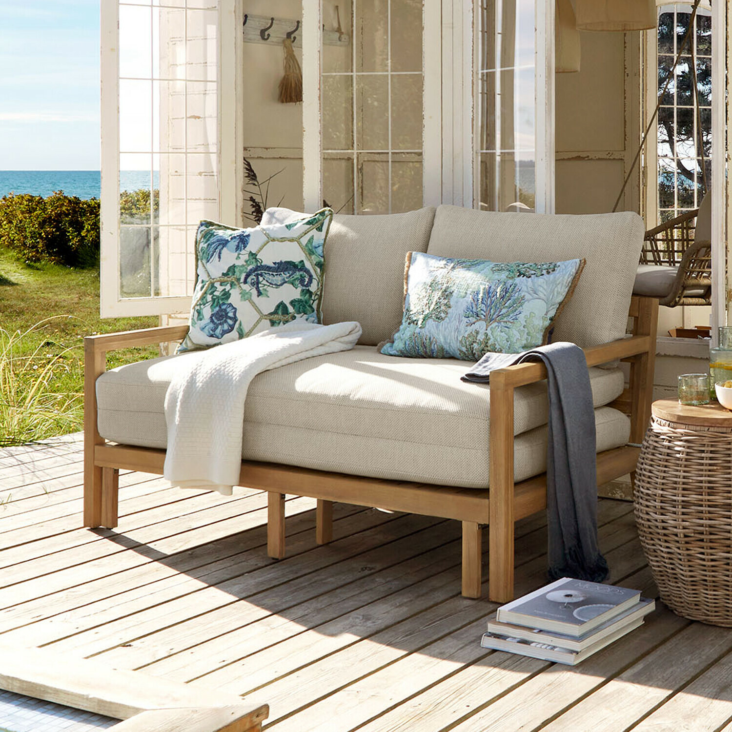 Sofá extraíble Tjorna Sofá beige claro con estructura de madera en terraza con vistas al jardín y al mar