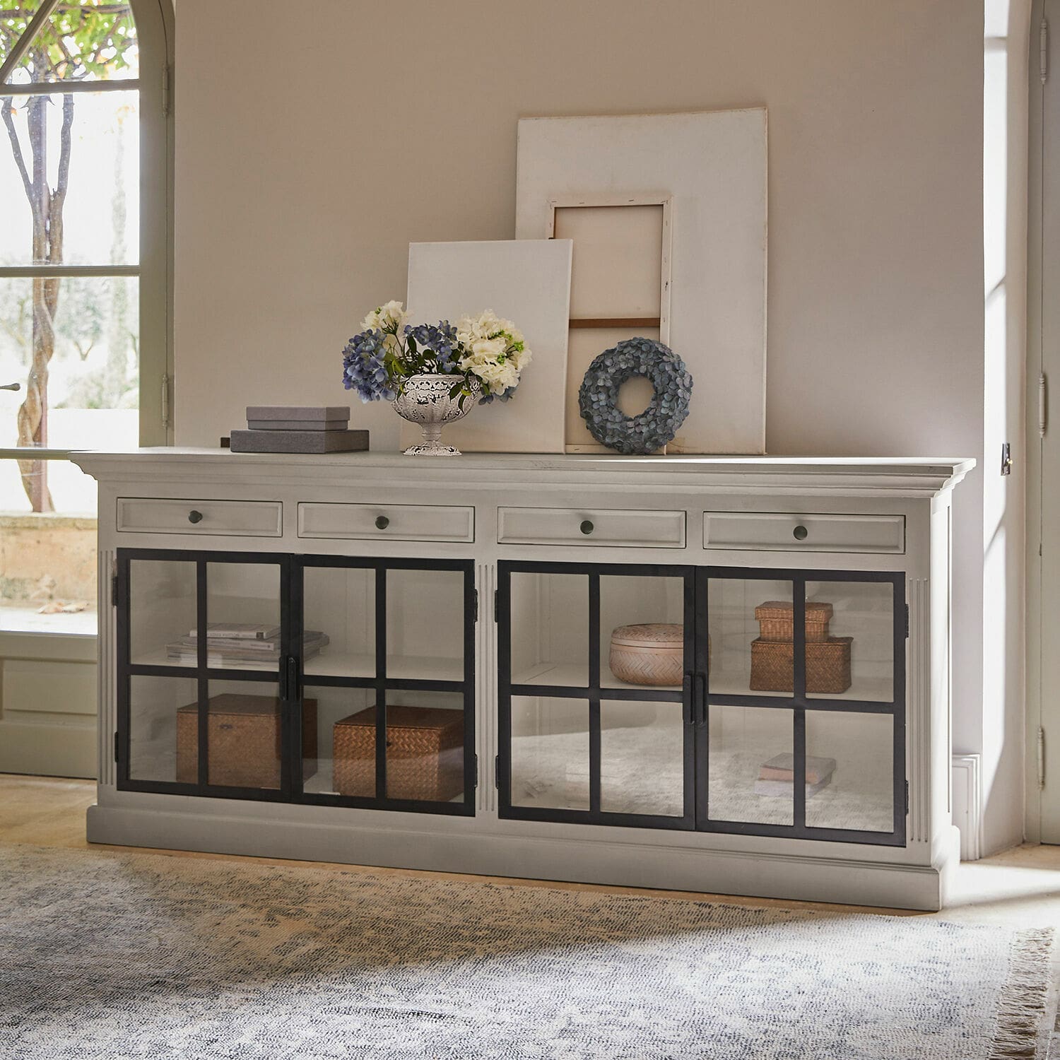 Cómoda Pratola Aparador de madera blanca con puertas de cristal negras y decoraciones encima en sala de estar