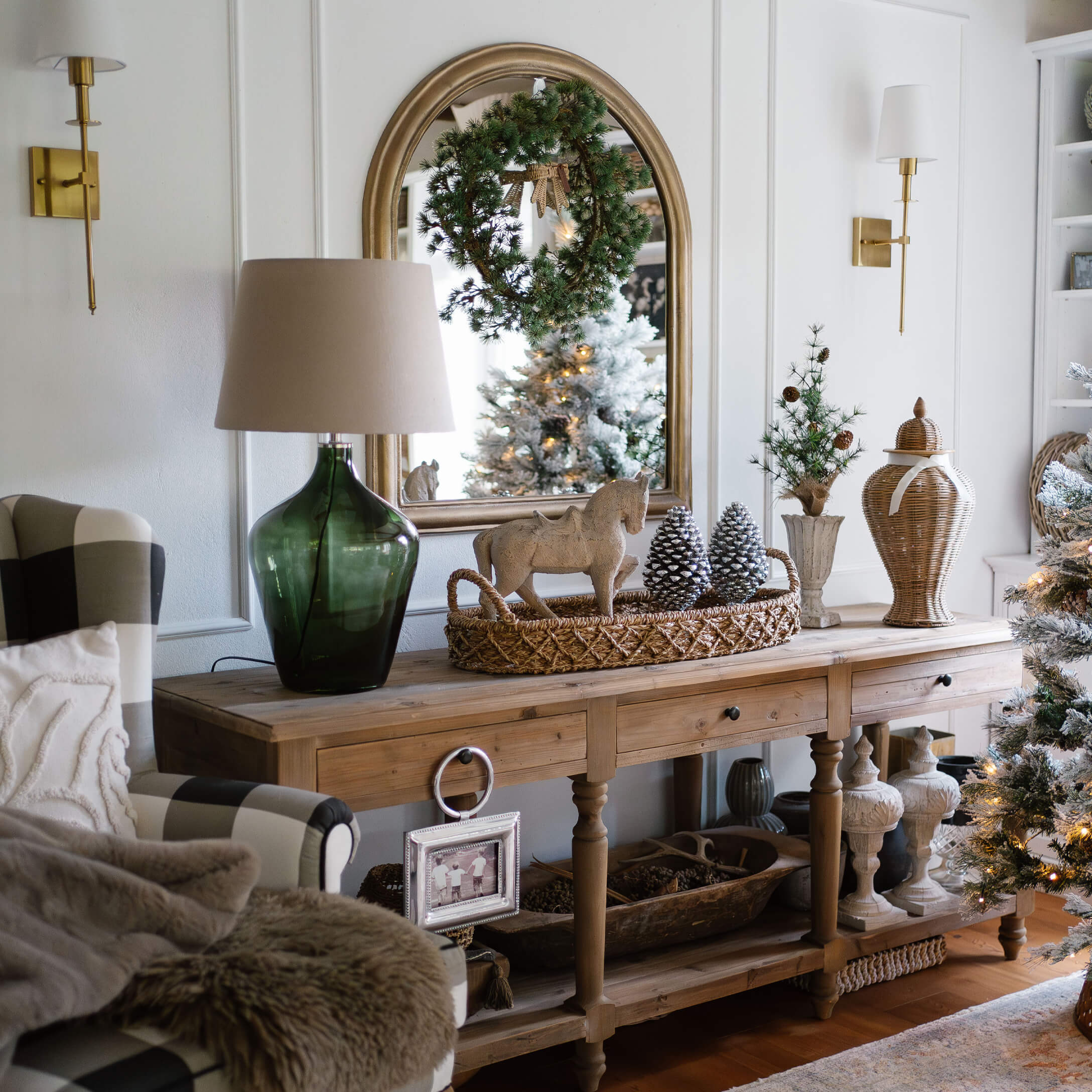Mesa de madera con decoración navideña, lámpara verde y espejo con corona en sala acogedora