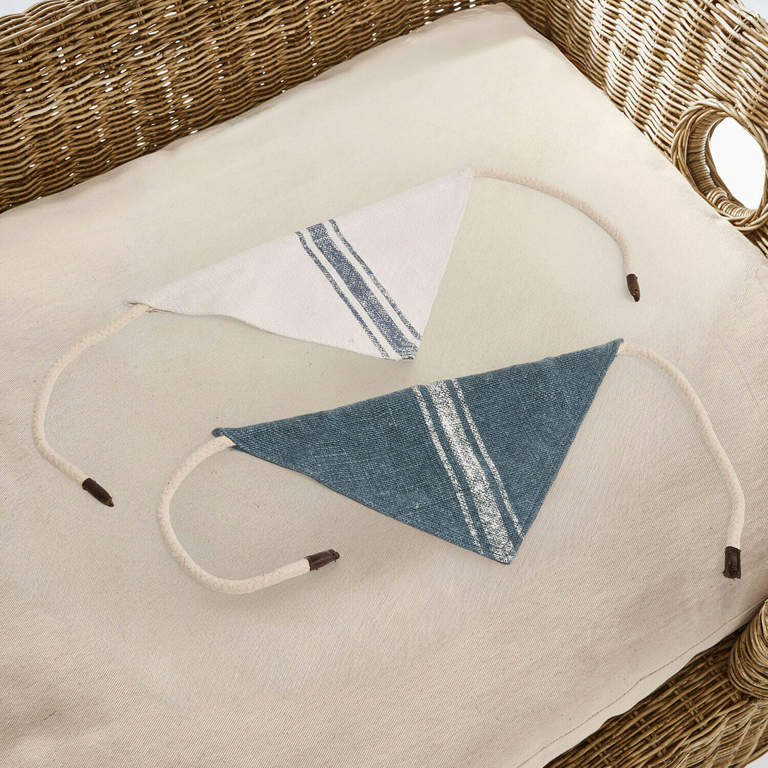 Set de 2 pañuelos para perros Pawera Dos protectores de hombro triangulares de algodón en blanco y azul con rayas sobre una silla de mimbre