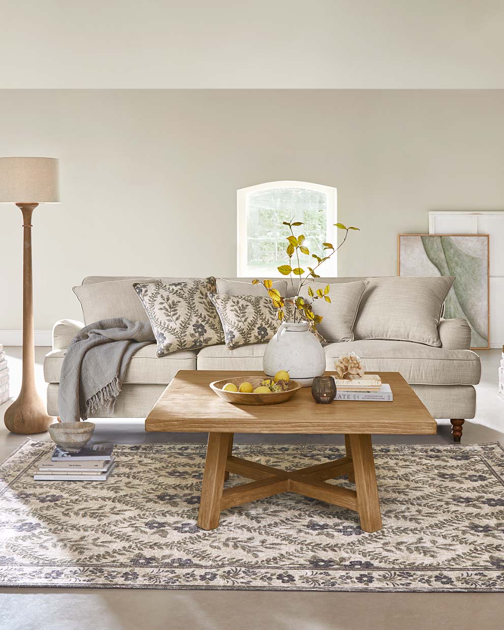 Salón acogedor con sofá beige, mesa de centro de madera y alfombra decorativa con diseño de hojas