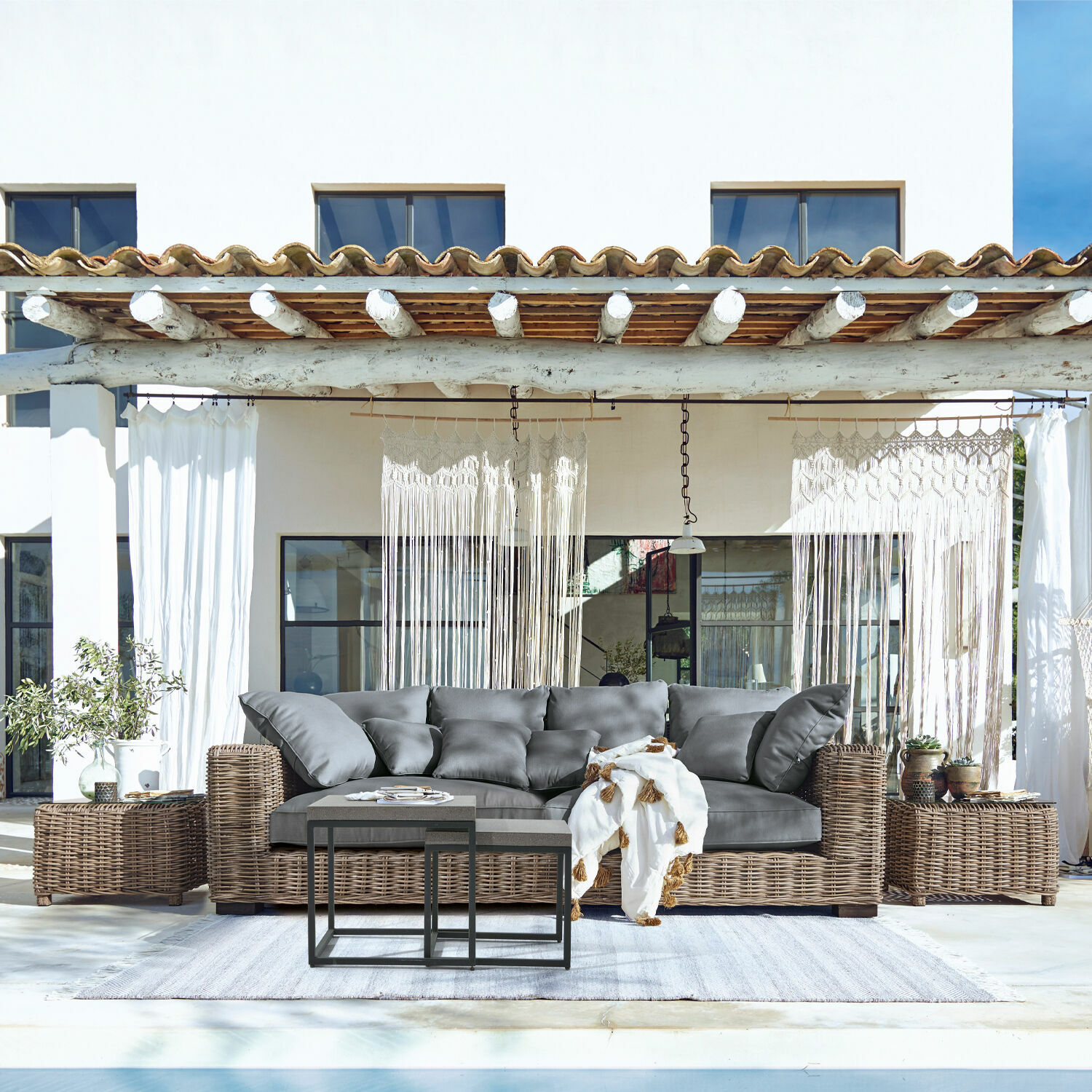 Sofa Rimini Sofá de ratán con cojines grises y mesas de centro metálicas en exterior junto a piscina, muebles de jardín
