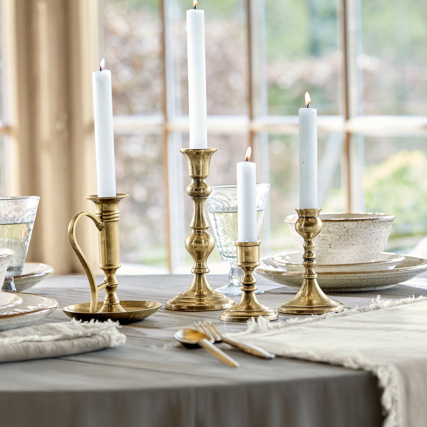 Set de 4 candeleros Maxéville Conjunto de cuatro candelabros de latón con velas blancas sobre mesa de madera en comedor