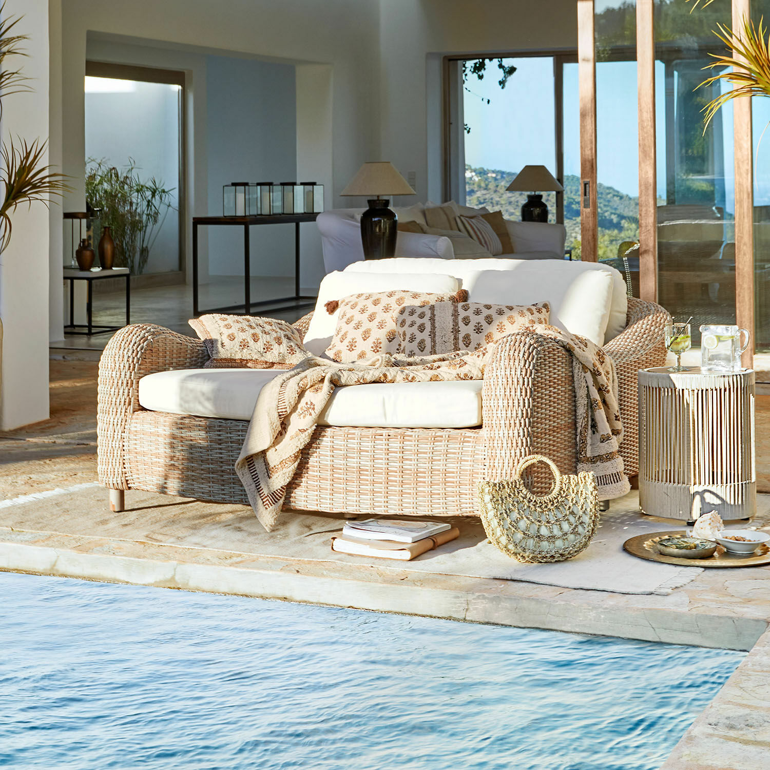 Tumbona Heloite Sofá de ratán natural con cojines crema y manta junto a la piscina en interior moderno