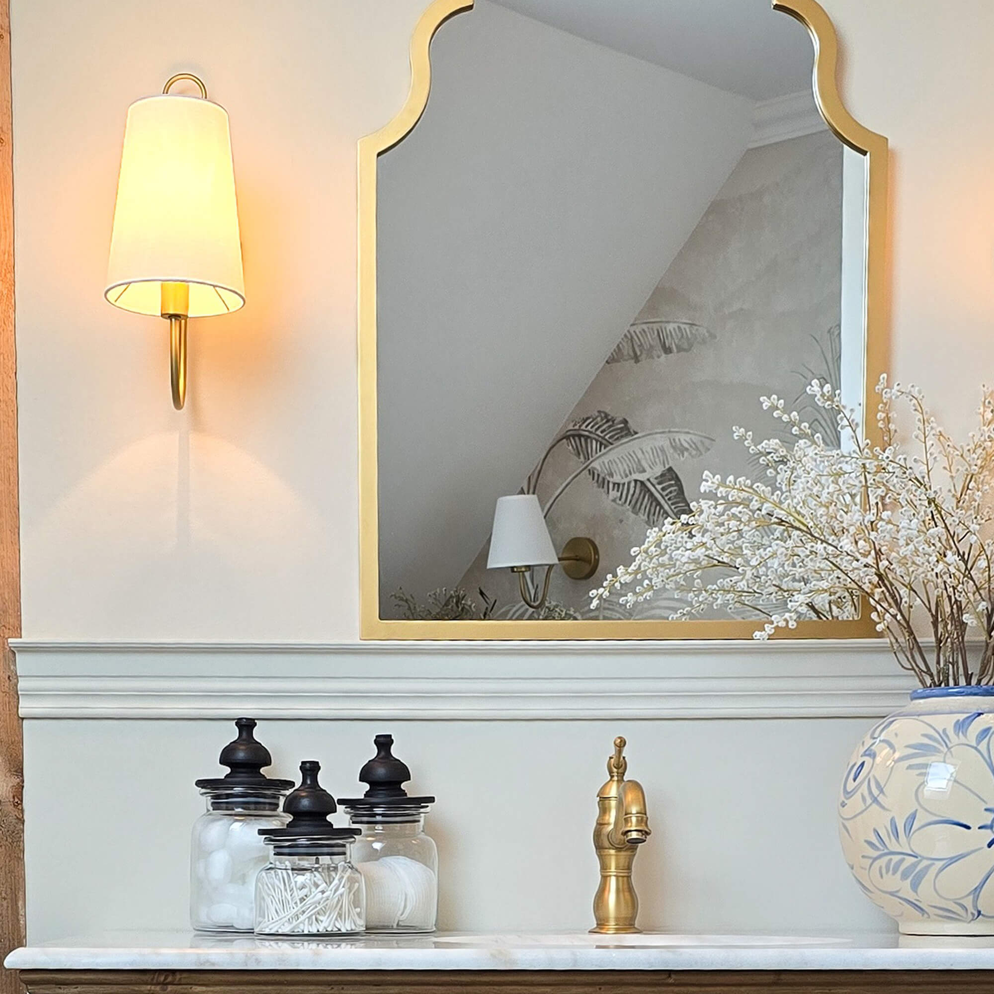 Espejo dorado con marco decorativo sobre lavabo de mármol con grifo de latón y frascos de vidrio
