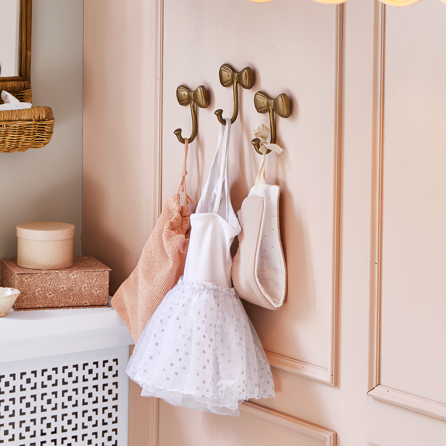 Ganchos metálicos dorados en forma de lazo en pared rosa con ropa infantil colgada