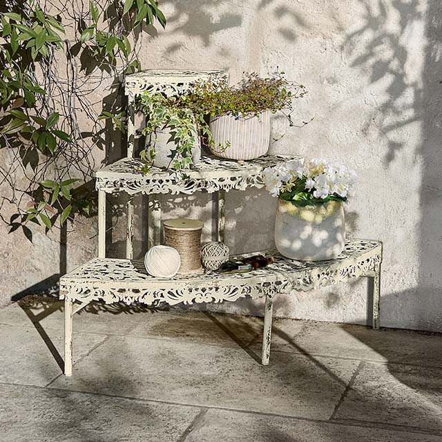 Estantería metálica crema con diseño calado, decorada con macetas y plantas para jardín