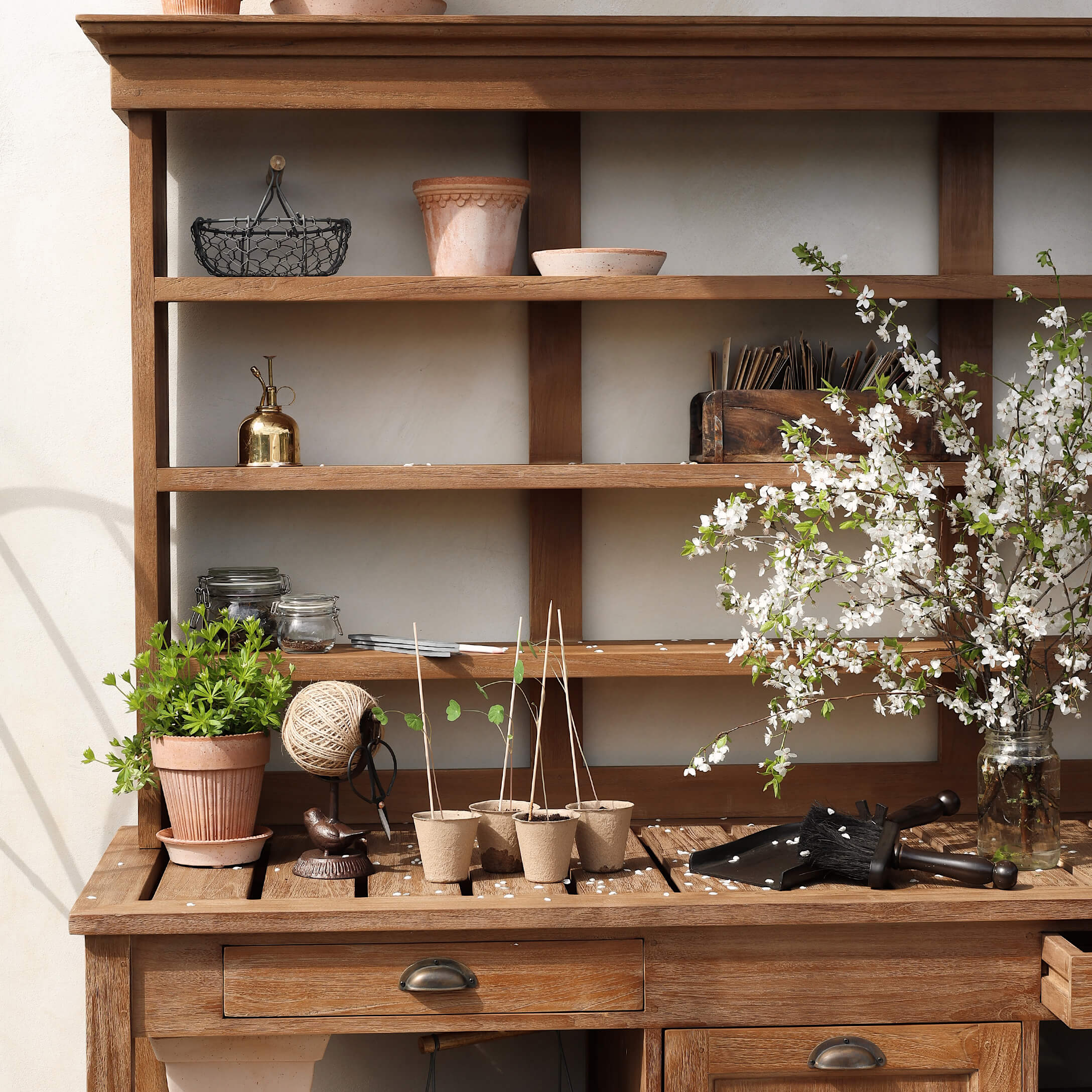 Mesa de jardín de madera con macetas, herramientas de jardinería y ramas florecidas en un frasco de vidrio