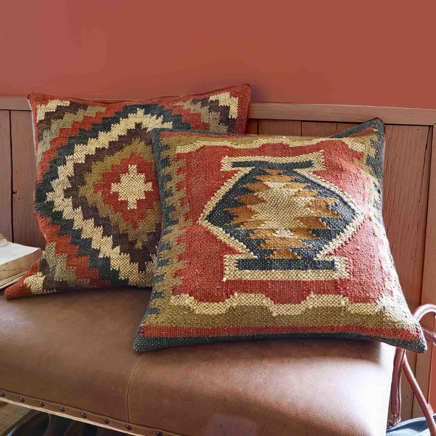 Dos cojines decorativos de tela con patrones geométricos en tonos cálidos rojo y beige sobre un sofá de cuero