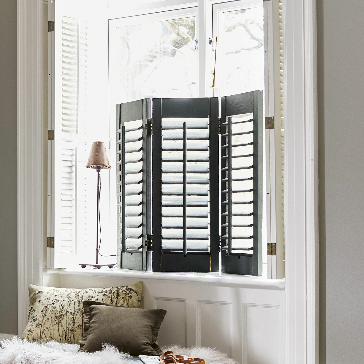 Biombo decorativo Ventura Persianas interiores negras de madera en ventana luminosa con cojines y lámpara en el alféizar