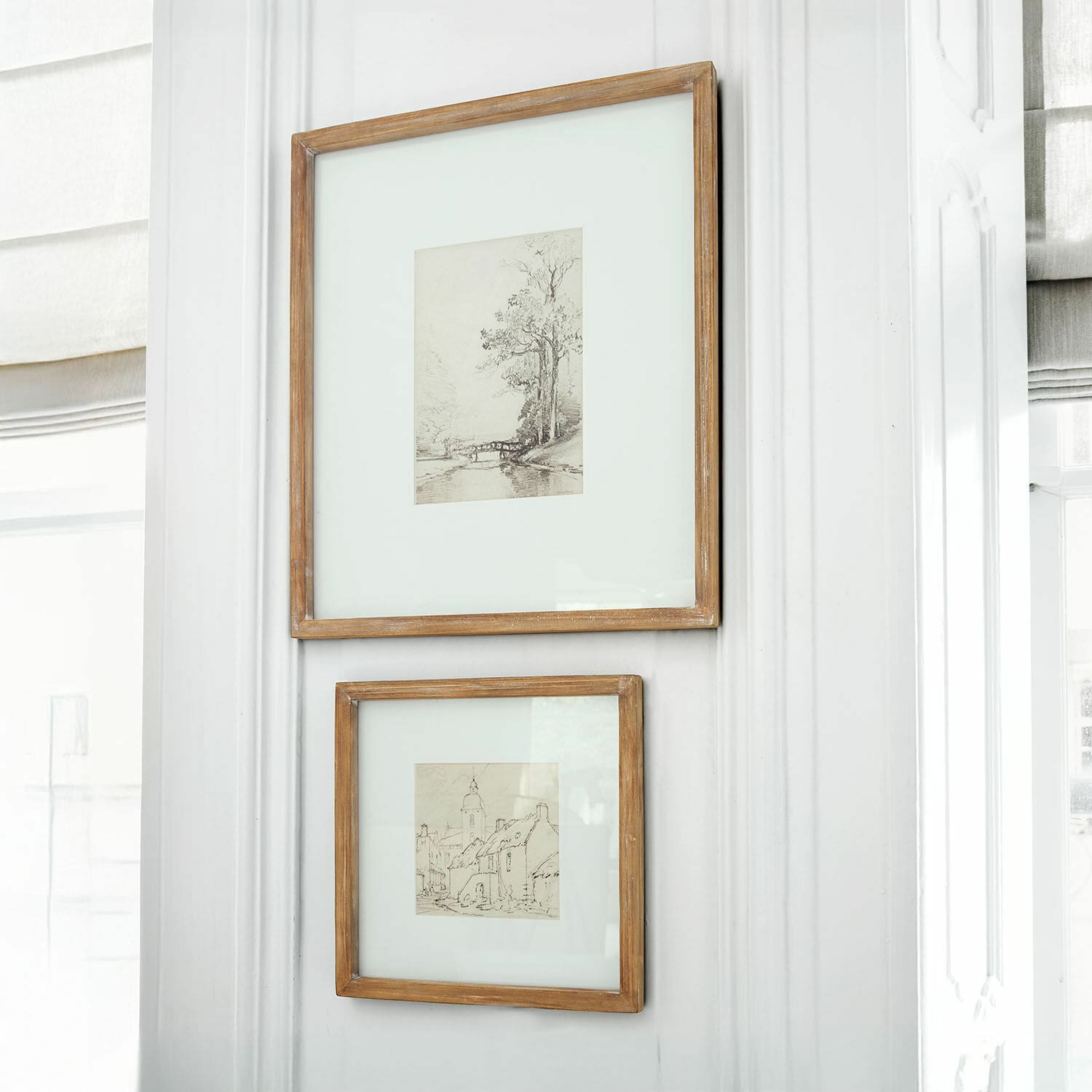 Set de 2 cuadros Juvarel Dos marcos de madera rústica con dibujos de paisajes colgados en pared blanca luminosa