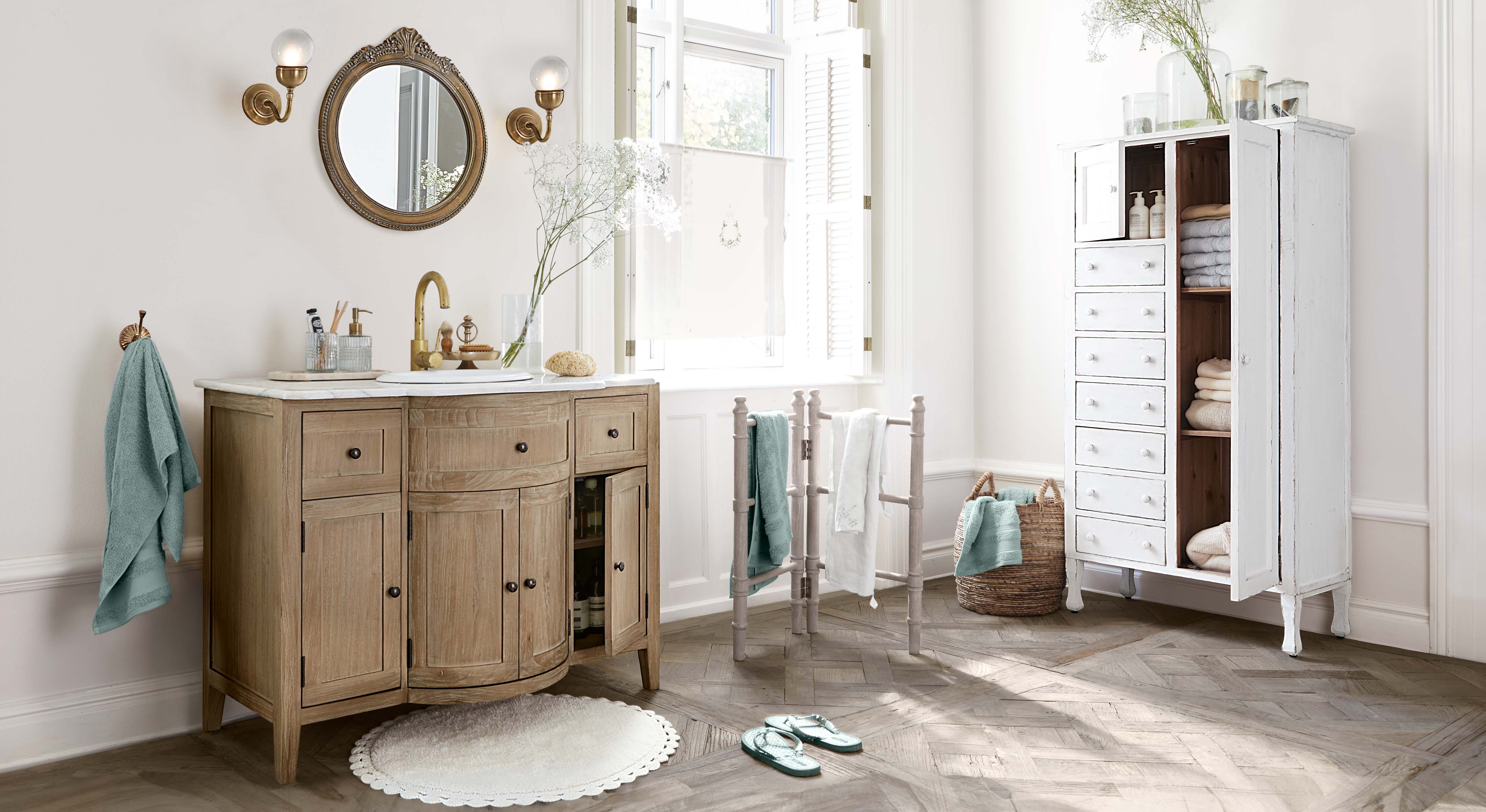 Baño con mueble de lavabo de madera, armario blanco y toallas turquesas, ambiente luminoso y natural